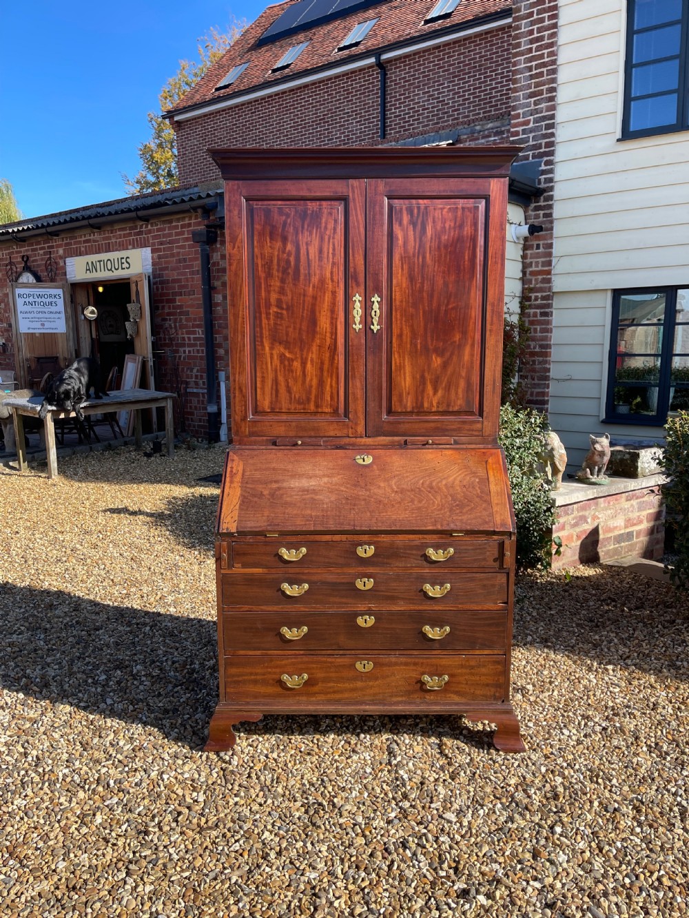 An eighteenth-century mahogany bureau bookcase featuring a two-door upper cabinet, slant-front desk, and four drawers with brass handles.