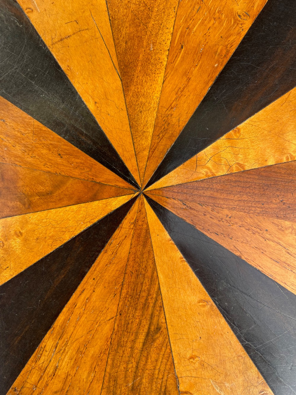 A circular Victorian specimen timber occasional table featuring a starburst parquetry top, a turned central pedestal stem, and three downswept tripod legs. View V