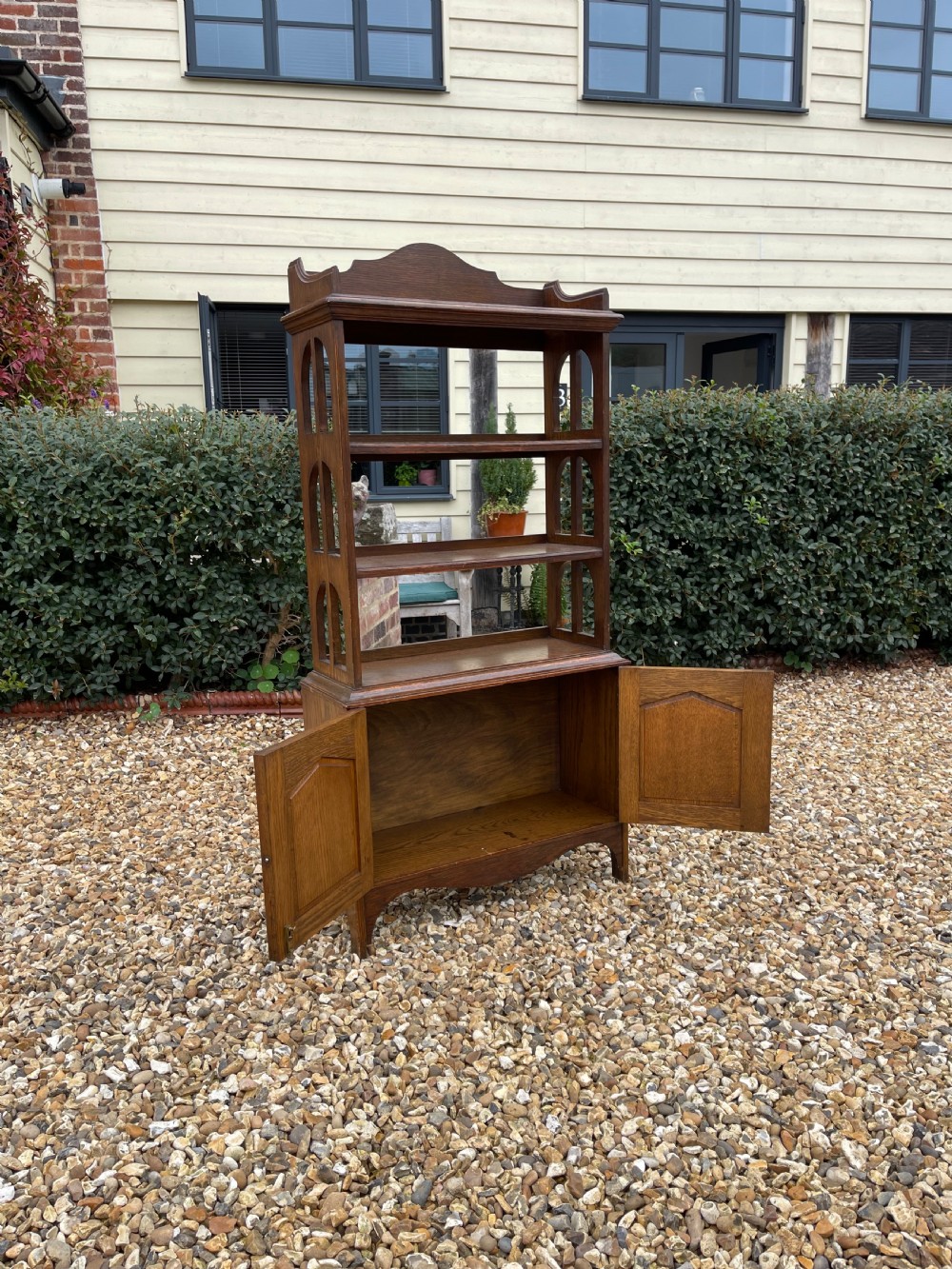 A freestanding oak open bookcase featuring two upper shelves with arched side cutouts over a lower two-door cupboard. View III