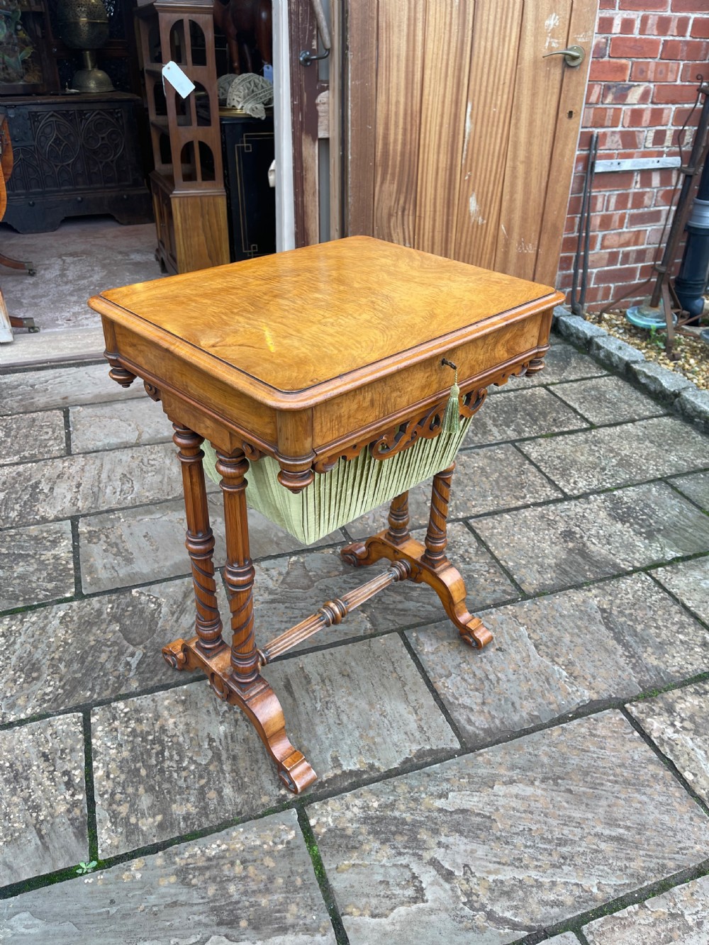 A Victorian burr walnut sewing work table with turned barley twist columns, a pleated green fabric basket, and a carved trestle base.