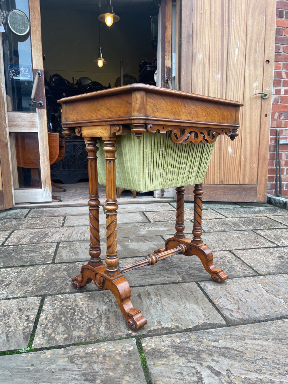 A Victorian burr walnut sewing work table with turned barley twist columns, a pleated green fabric basket, and a carved trestle base. View III