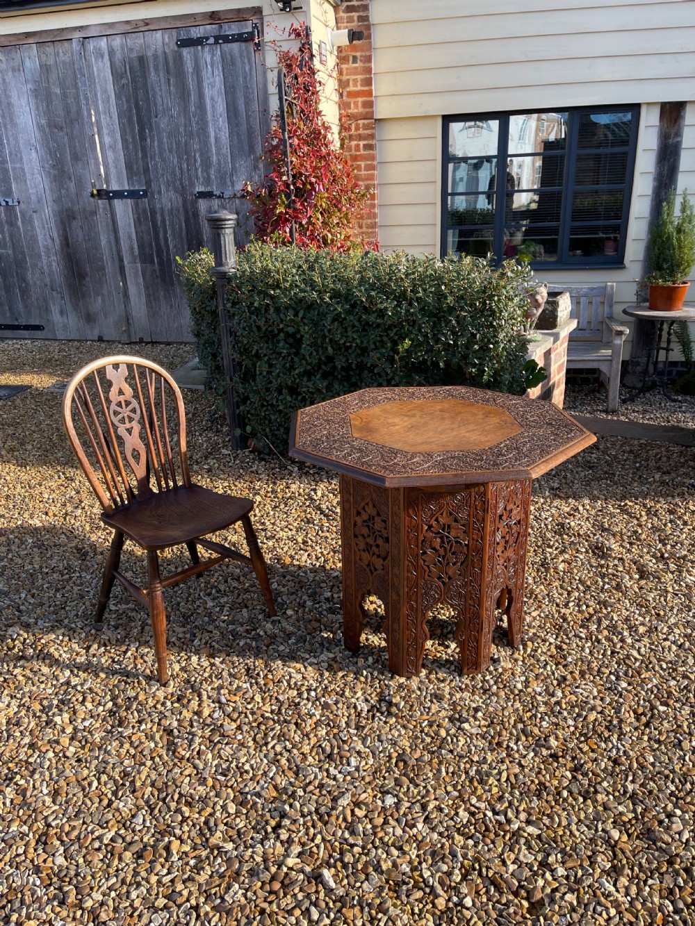 An octagonal dark walnut table featuring detailed botanical relief carving on the tabletop and pierced arched side panels.
