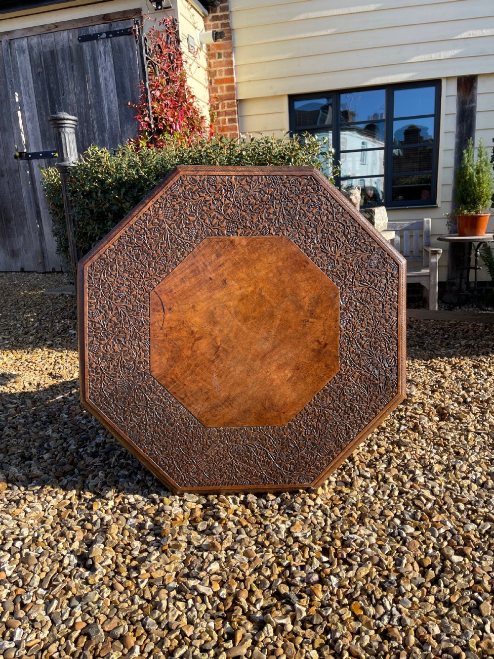 An octagonal dark walnut table featuring detailed botanical relief carving on the tabletop and pierced arched side panels. View II