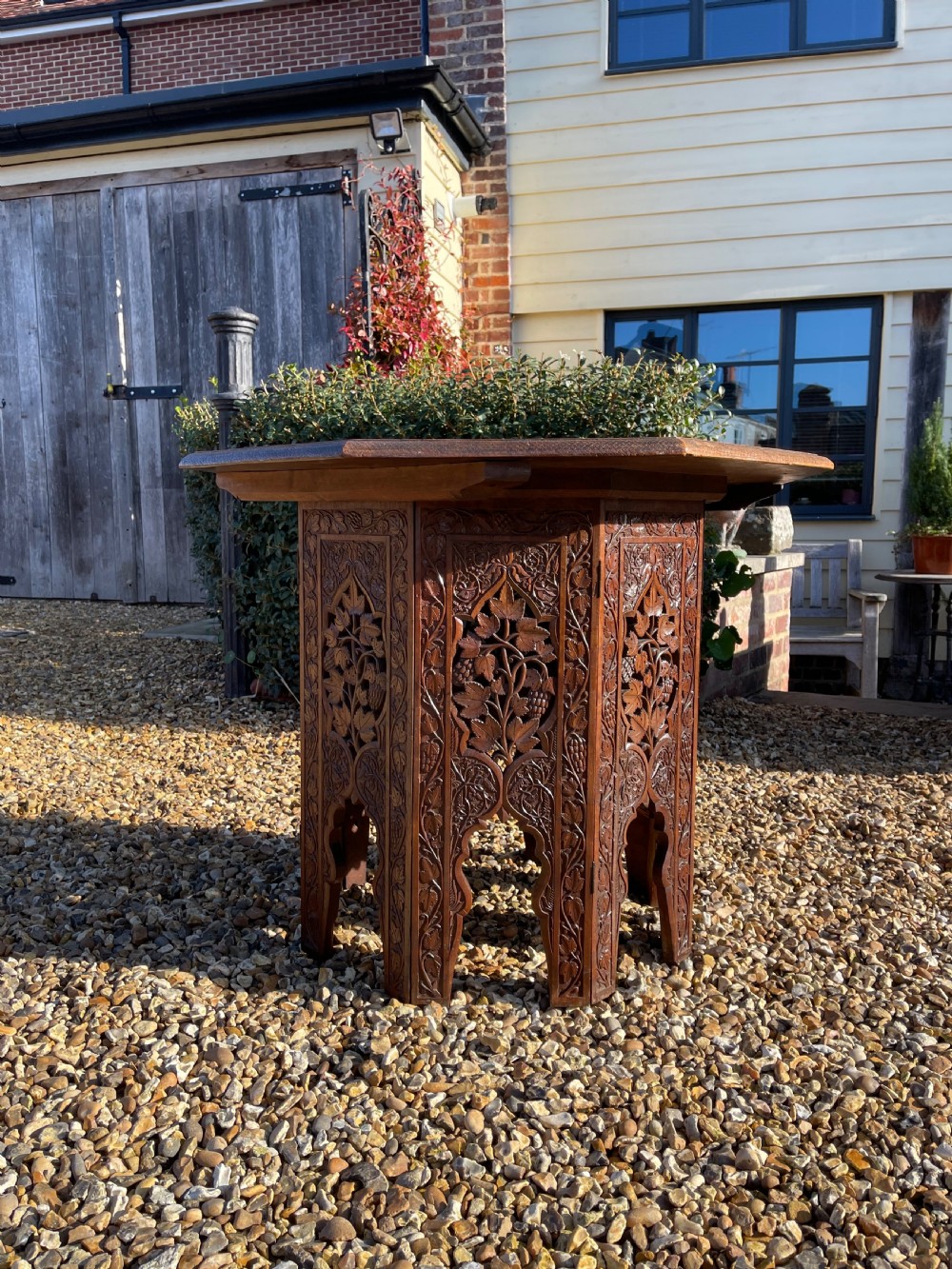 An octagonal dark walnut table featuring detailed botanical relief carving on the tabletop and pierced arched side panels. View V