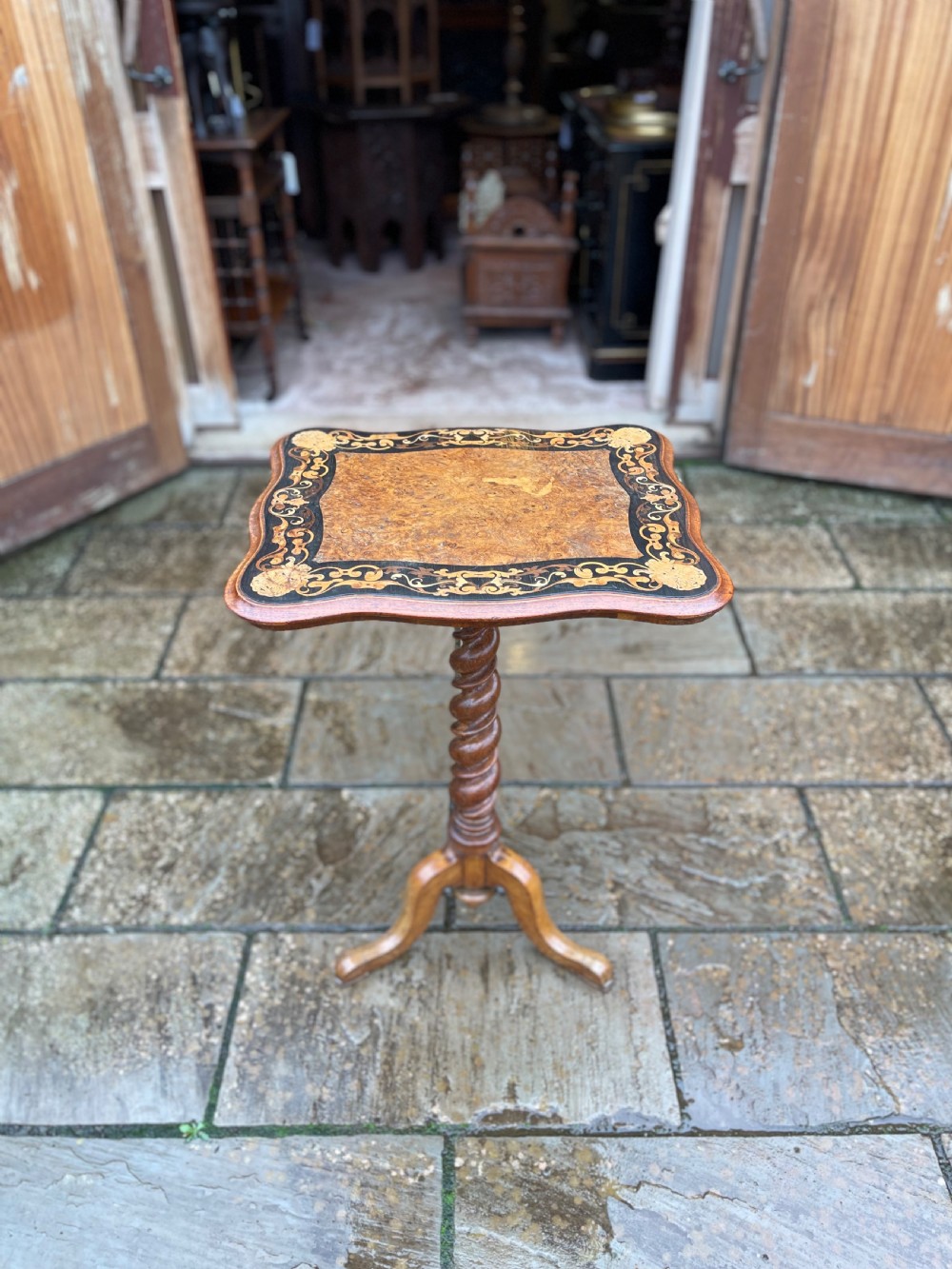 A nineteenth-century burr walnut occasional table featuring a shaped top with intricate floral marquetry, supported by a central barley twist column and a tripod base.