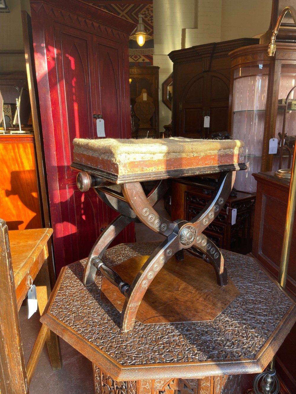 Victorian Aesthetic Movement ebonised x-frame stool featuring incised circular motifs, side adjustment knobs, and a neutral fabric seat.
