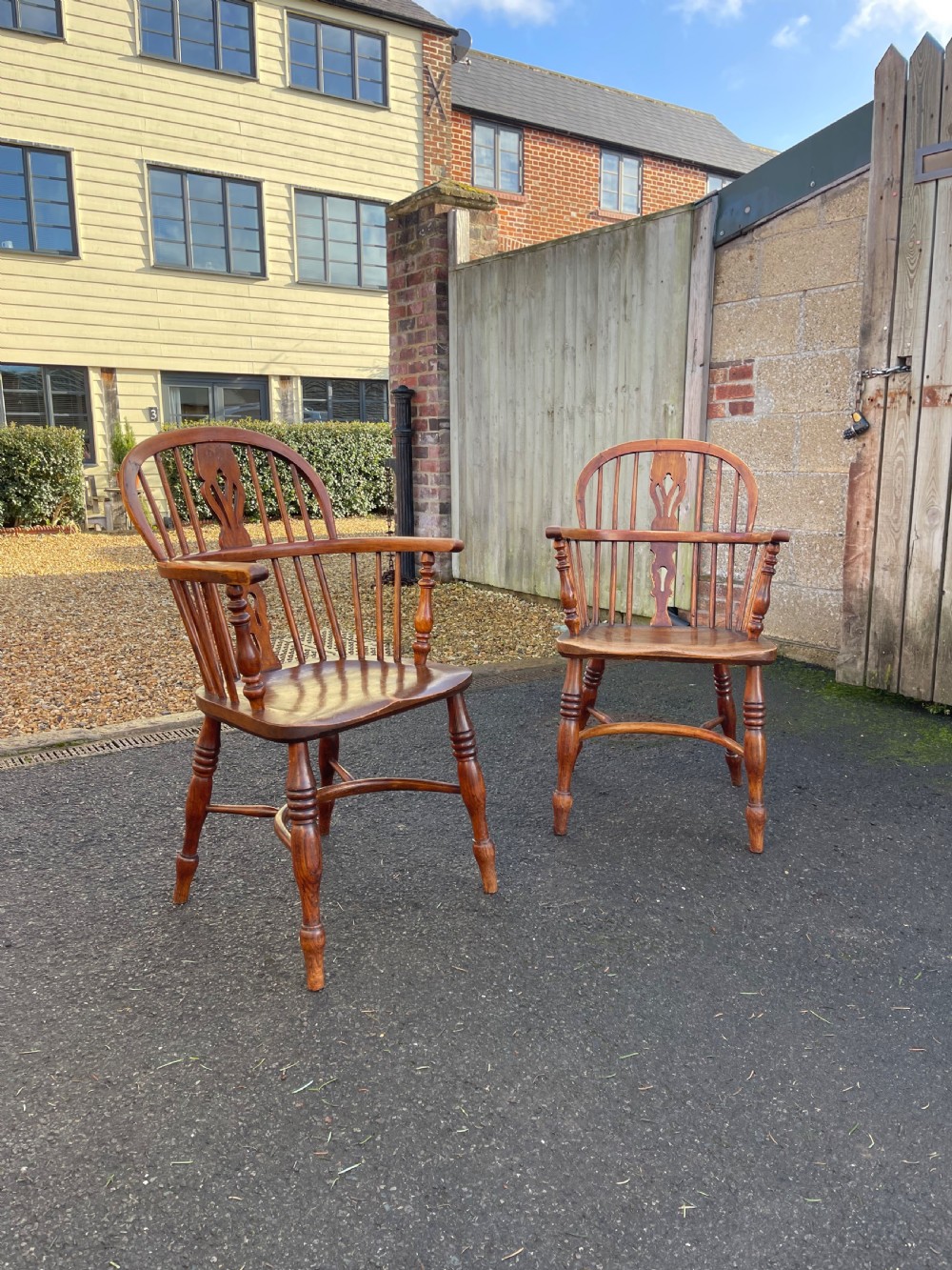 A pair of warm brown wooden Windsor armchairs featuring hoop backs, pierced central splats, turned legs, and curved stretchers.