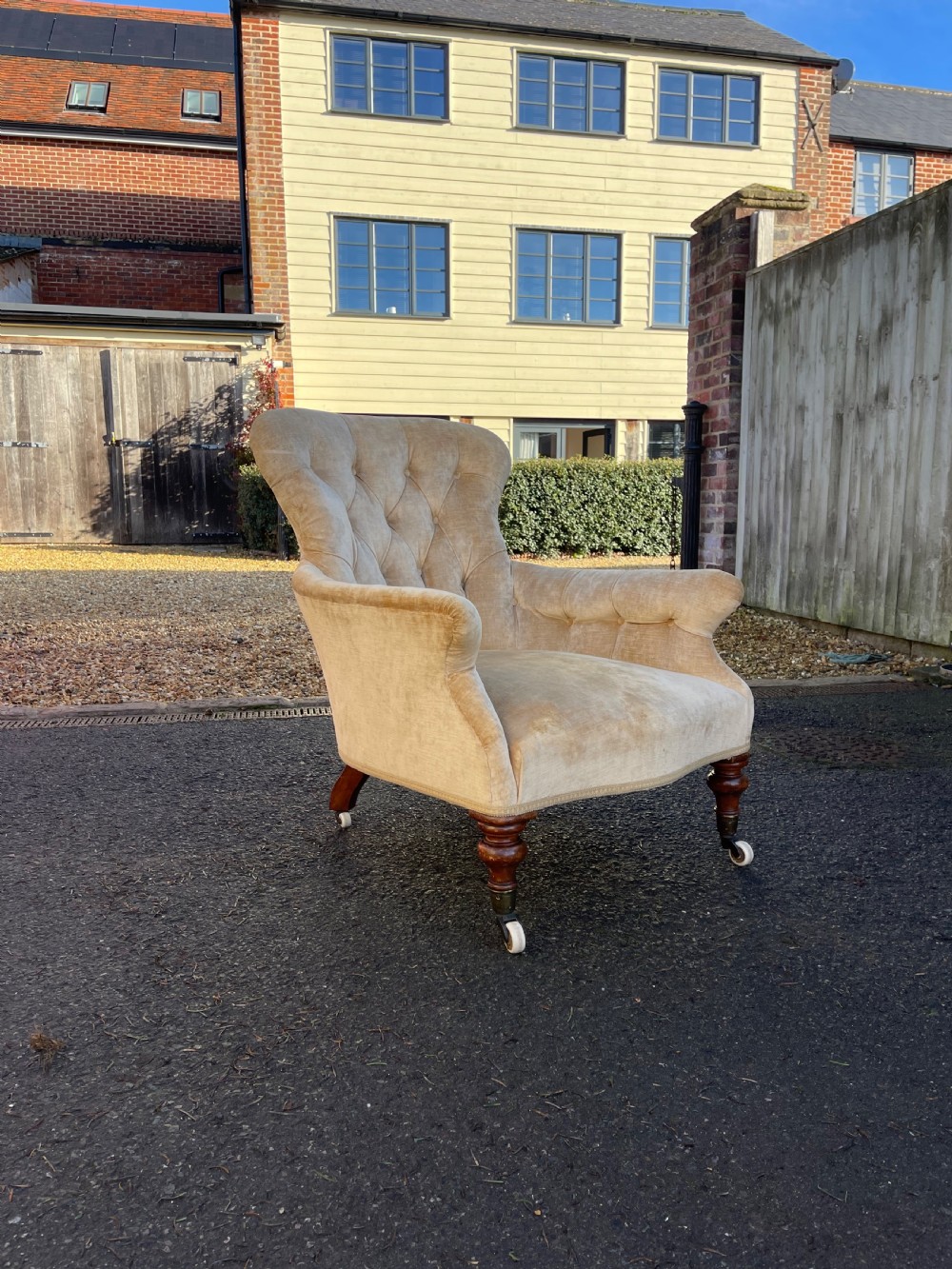 A nineteenth-century Victorian button-back armchair upholstered in beige velvet with scroll arms and turned mahogany legs on white castors.