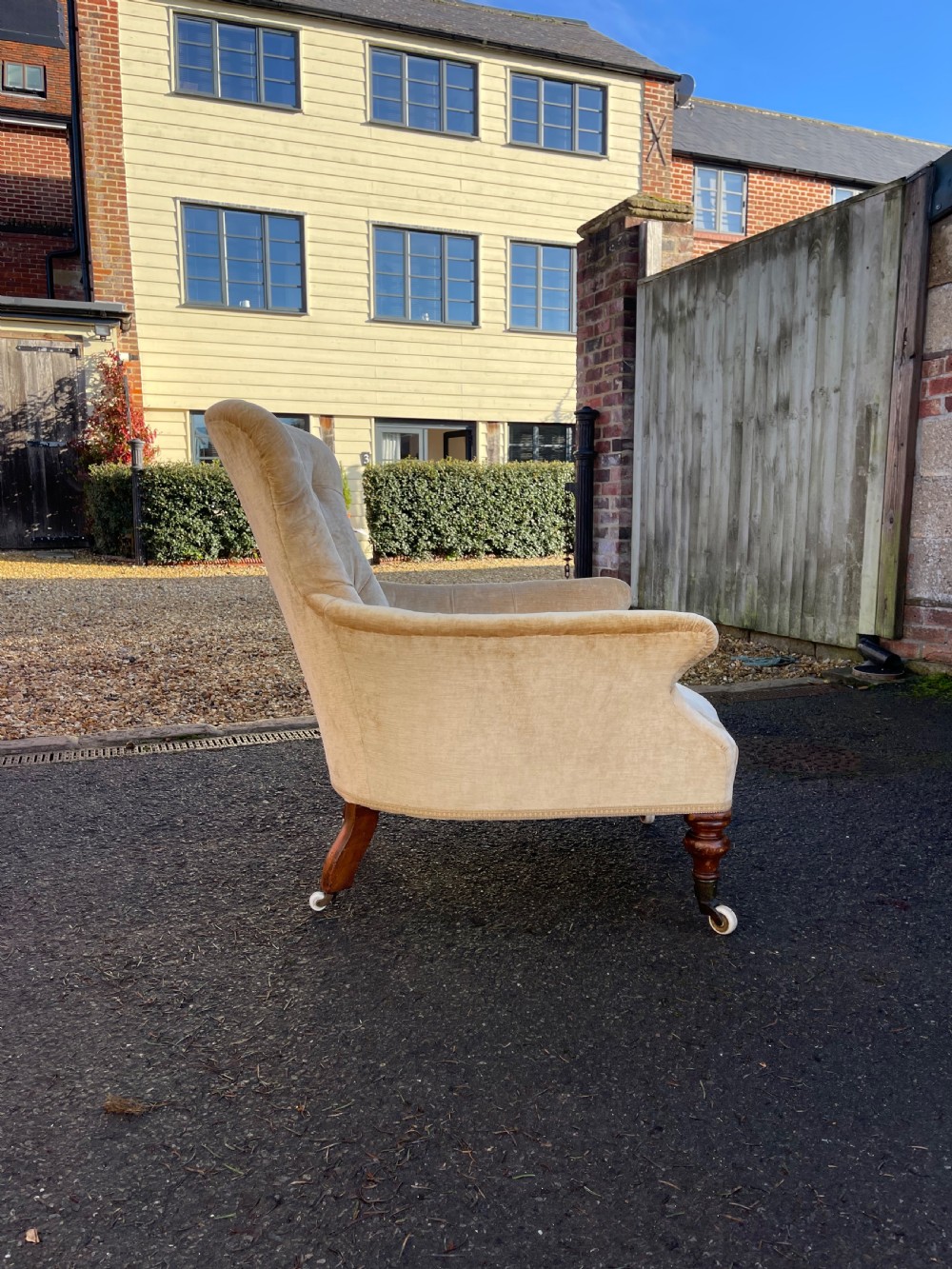 A nineteenth-century Victorian button-back armchair upholstered in beige velvet with scroll arms and turned mahogany legs on white castors. View II