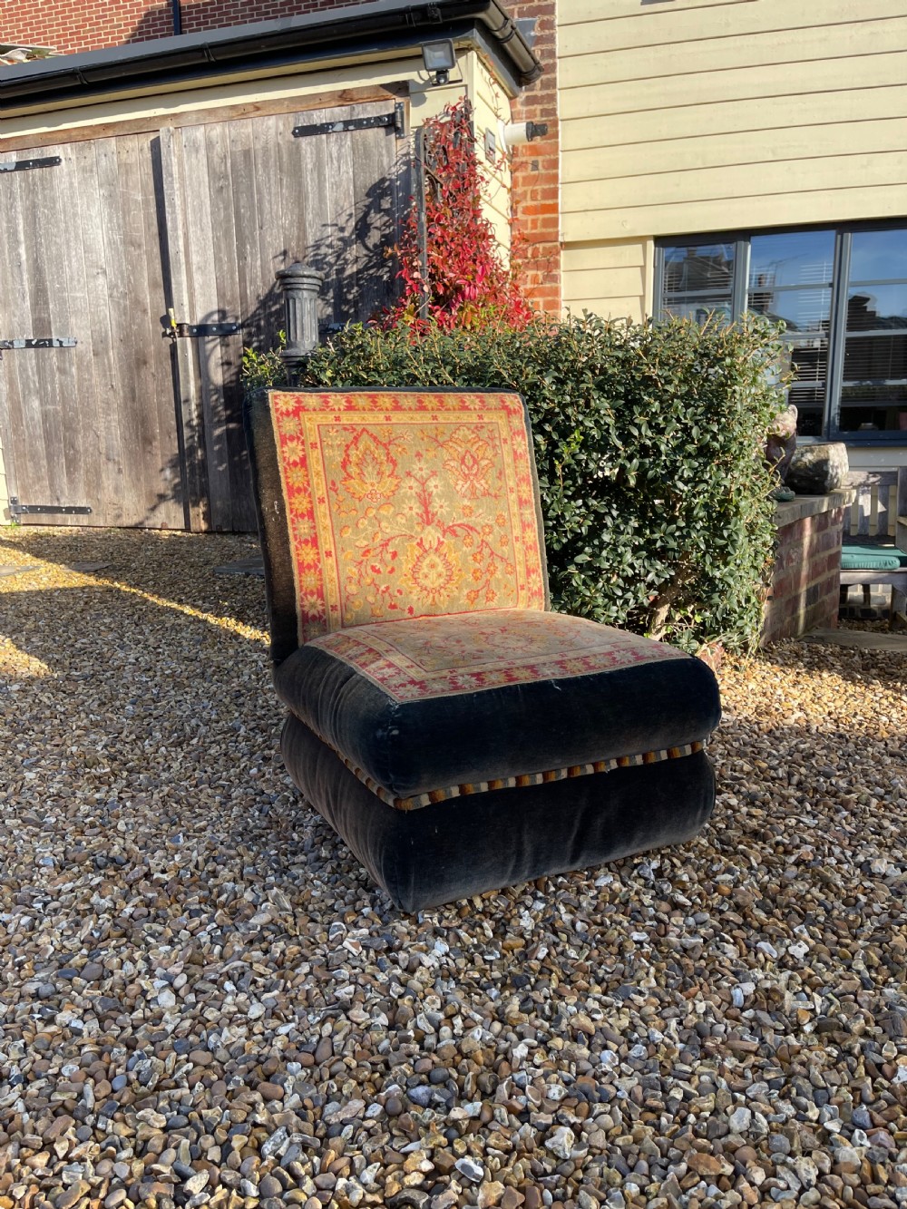 An armless slipper chair upholstered in dark charcoal velvet with a central panel featuring a red and gold oriental carpet pattern.