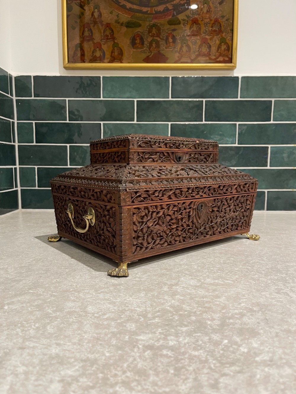 An intricately carved brown sandalwood jewellery box with a stepped lid, brass side drop handles, and brass claw feet.