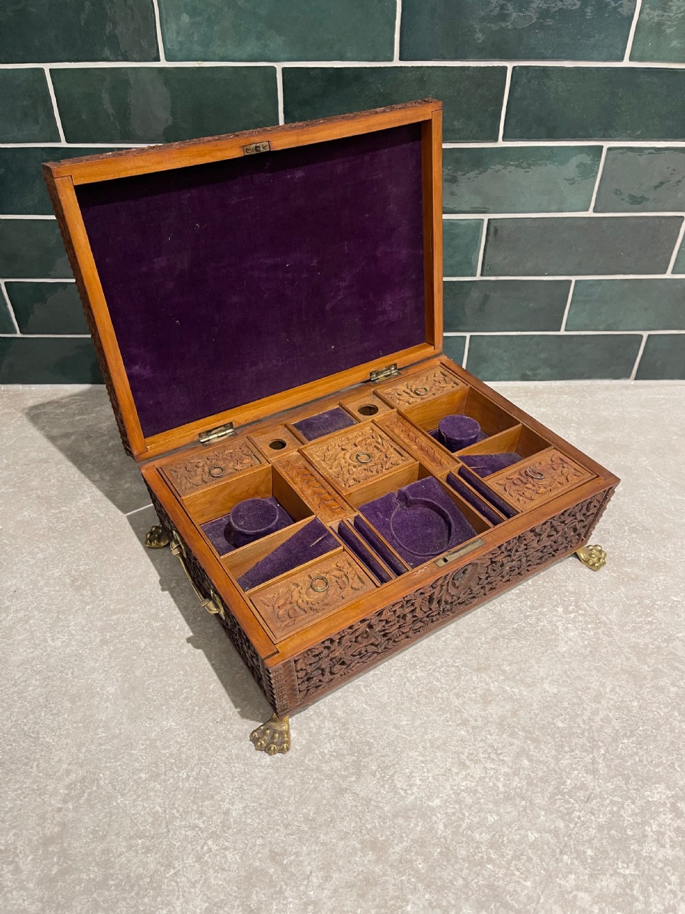 An intricately carved brown sandalwood jewellery box with a stepped lid, brass side drop handles, and brass claw feet. View VI