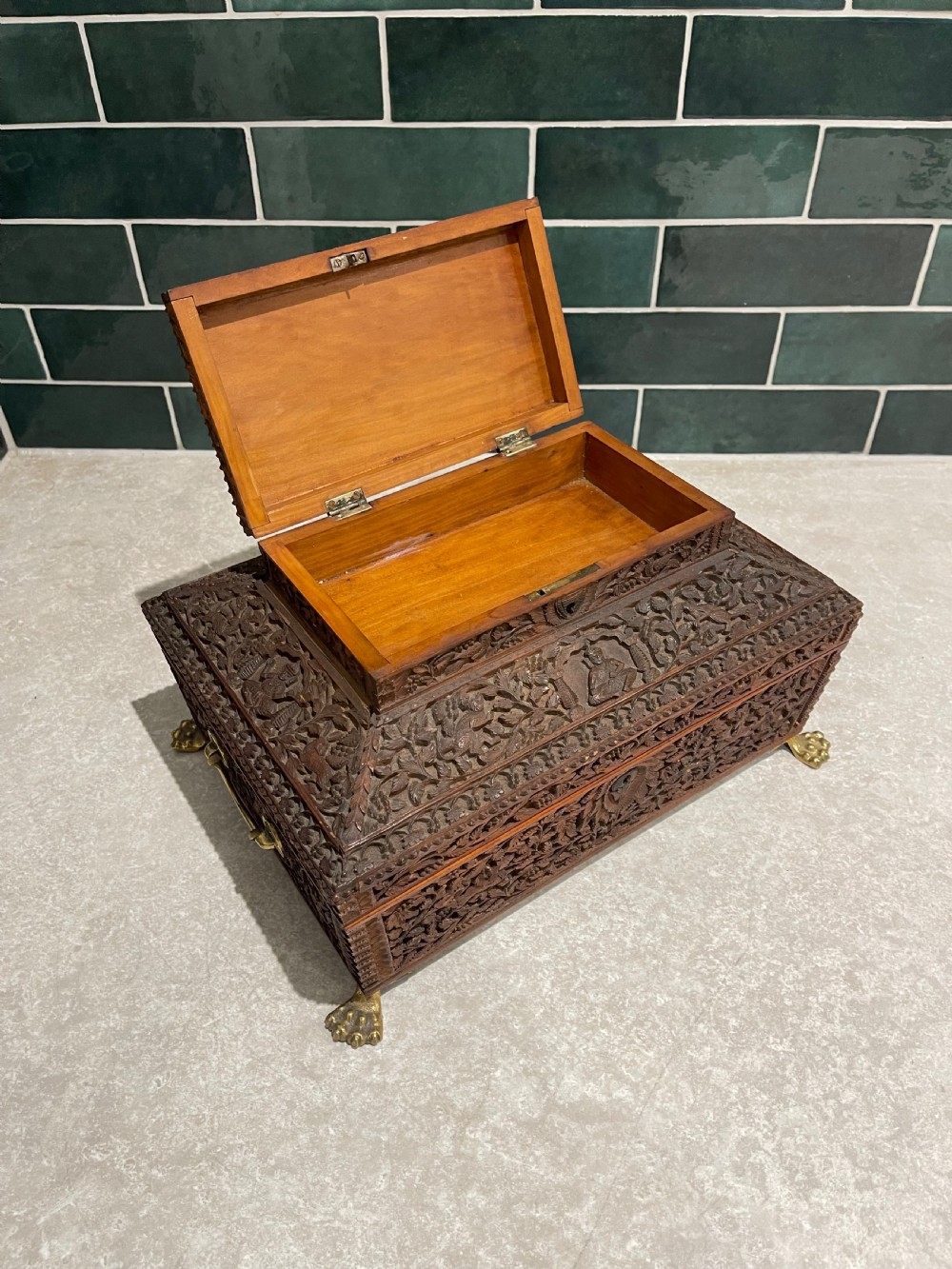 An intricately carved brown sandalwood jewellery box with a stepped lid, brass side drop handles, and brass claw feet. View VII