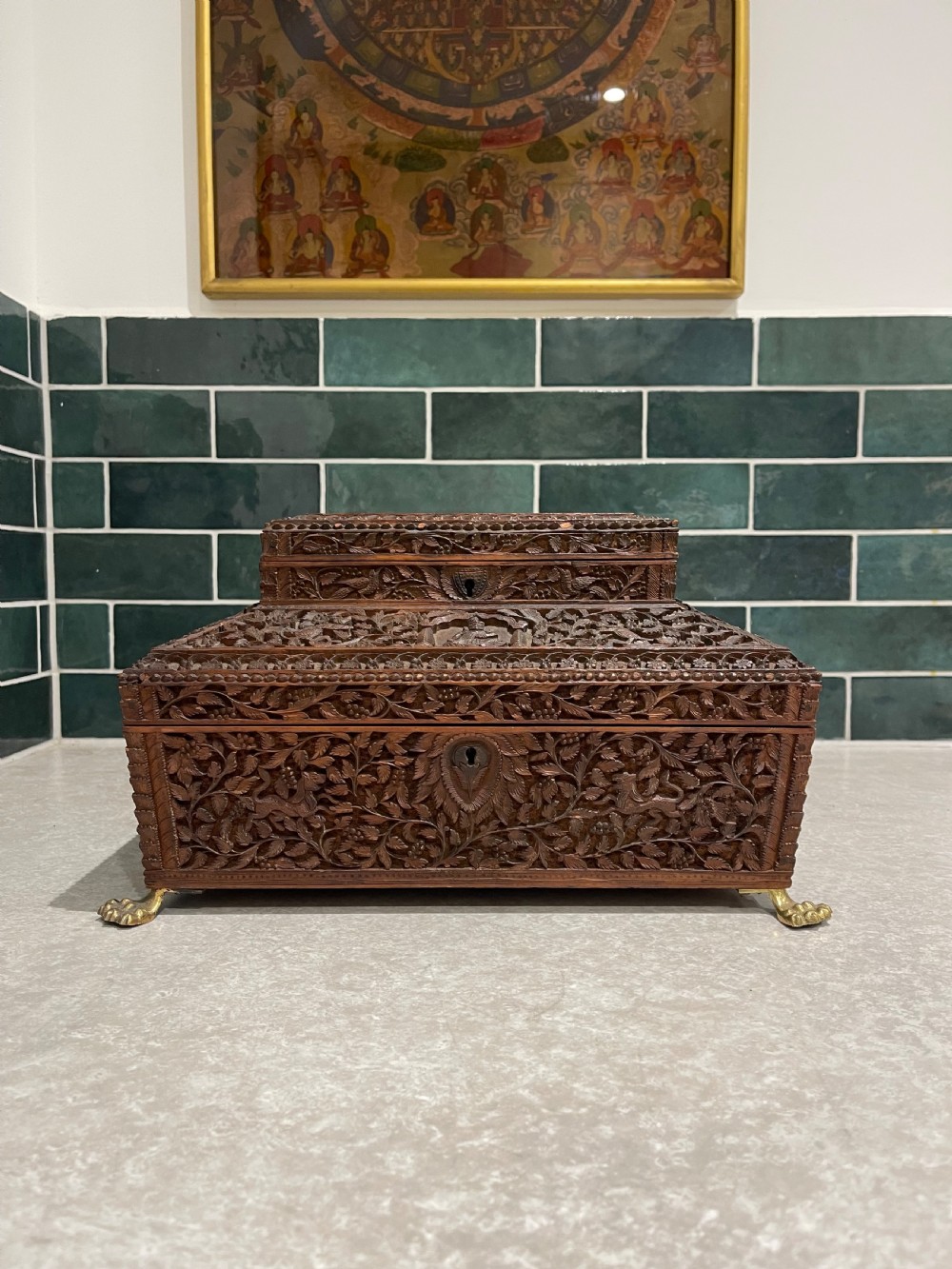An intricately carved brown sandalwood jewellery box with a stepped lid, brass side drop handles, and brass claw feet. View X