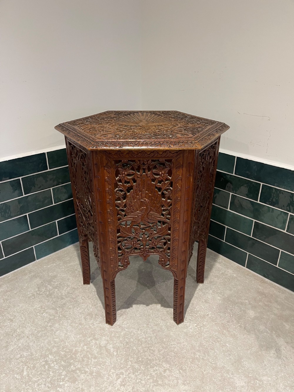 A dark hardwood hexagonal side table featuring intricate hand-carved floral fretwork and pierced side panels with peacock motifs.