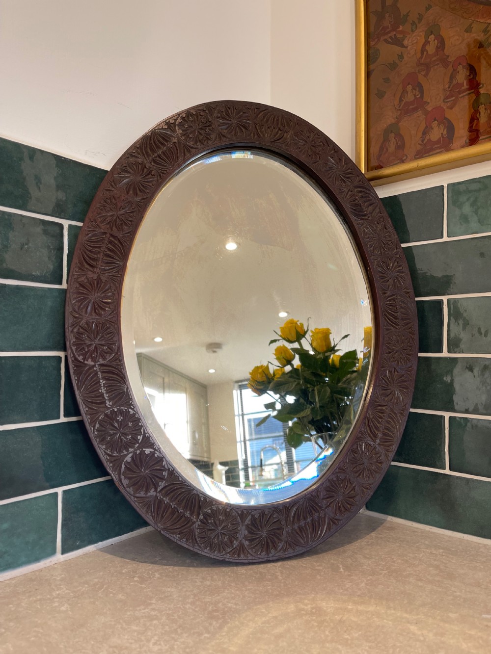 An oval wall mirror featuring a dark brown wooden frame decorated with detailed geometric chip-carved rosette patterns.