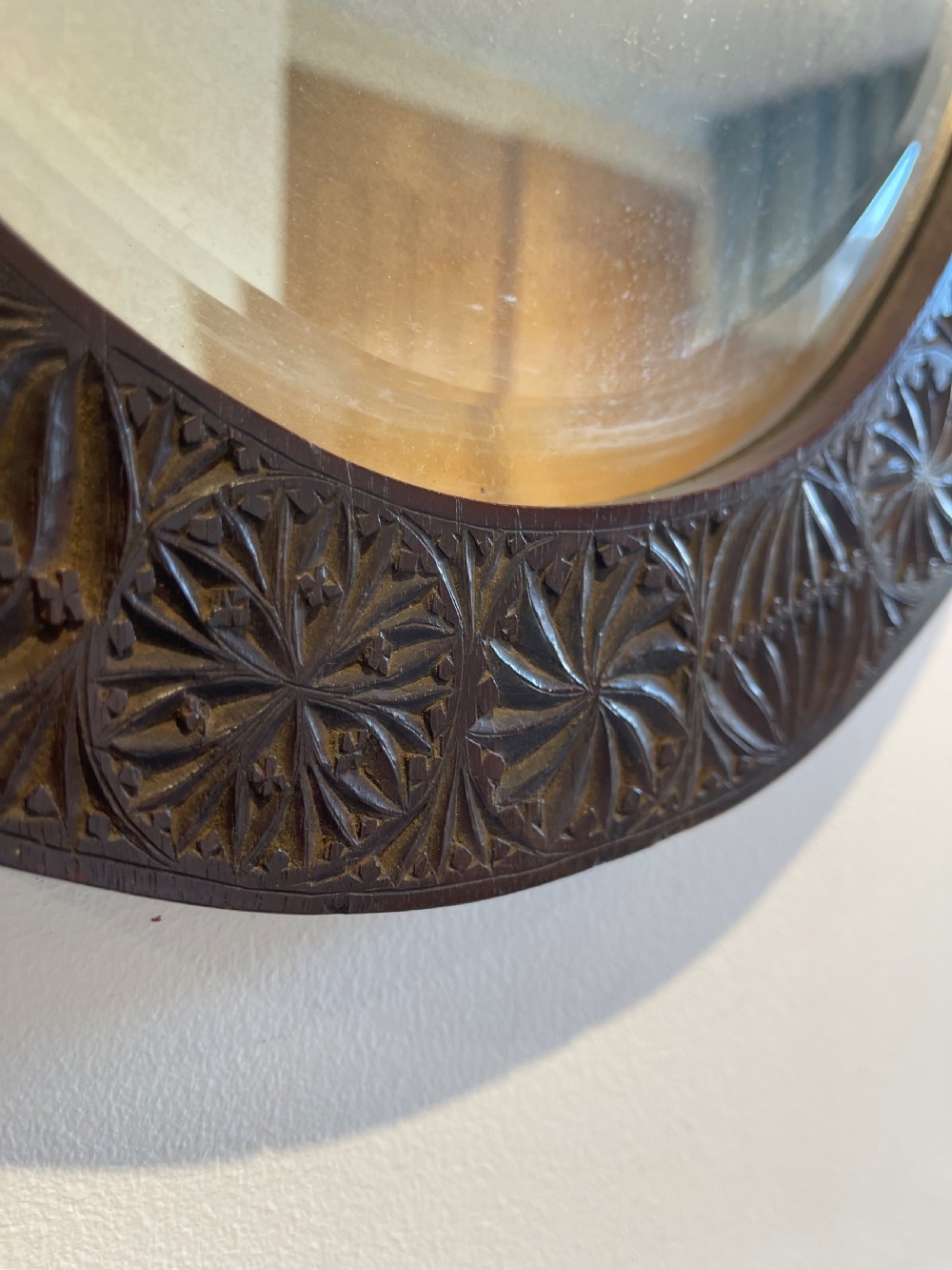 An oval wall mirror featuring a dark brown wooden frame decorated with detailed geometric chip-carved rosette patterns. View III