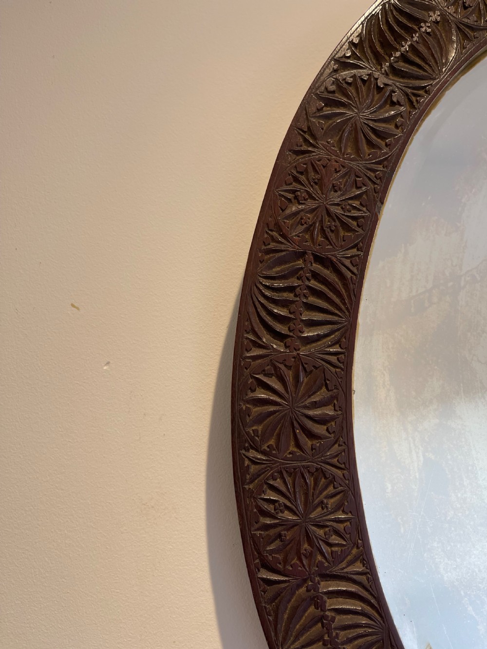 An oval wall mirror featuring a dark brown wooden frame decorated with detailed geometric chip-carved rosette patterns. View IV