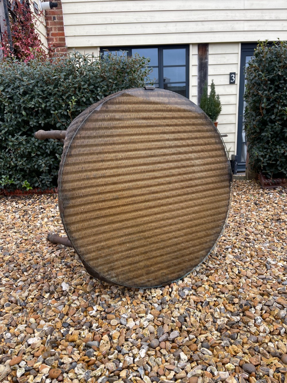 A round dark brown Lloyd Loom table featuring a circular glass top protective surface, flared woven legs, and a lower central woven shelf. View II