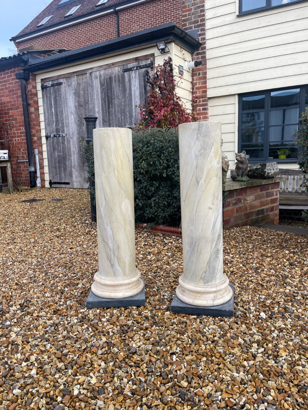 A pair of tall cylindrical plaster pedestals painted with a faux-marble finish on square dark grey plinth bases.
