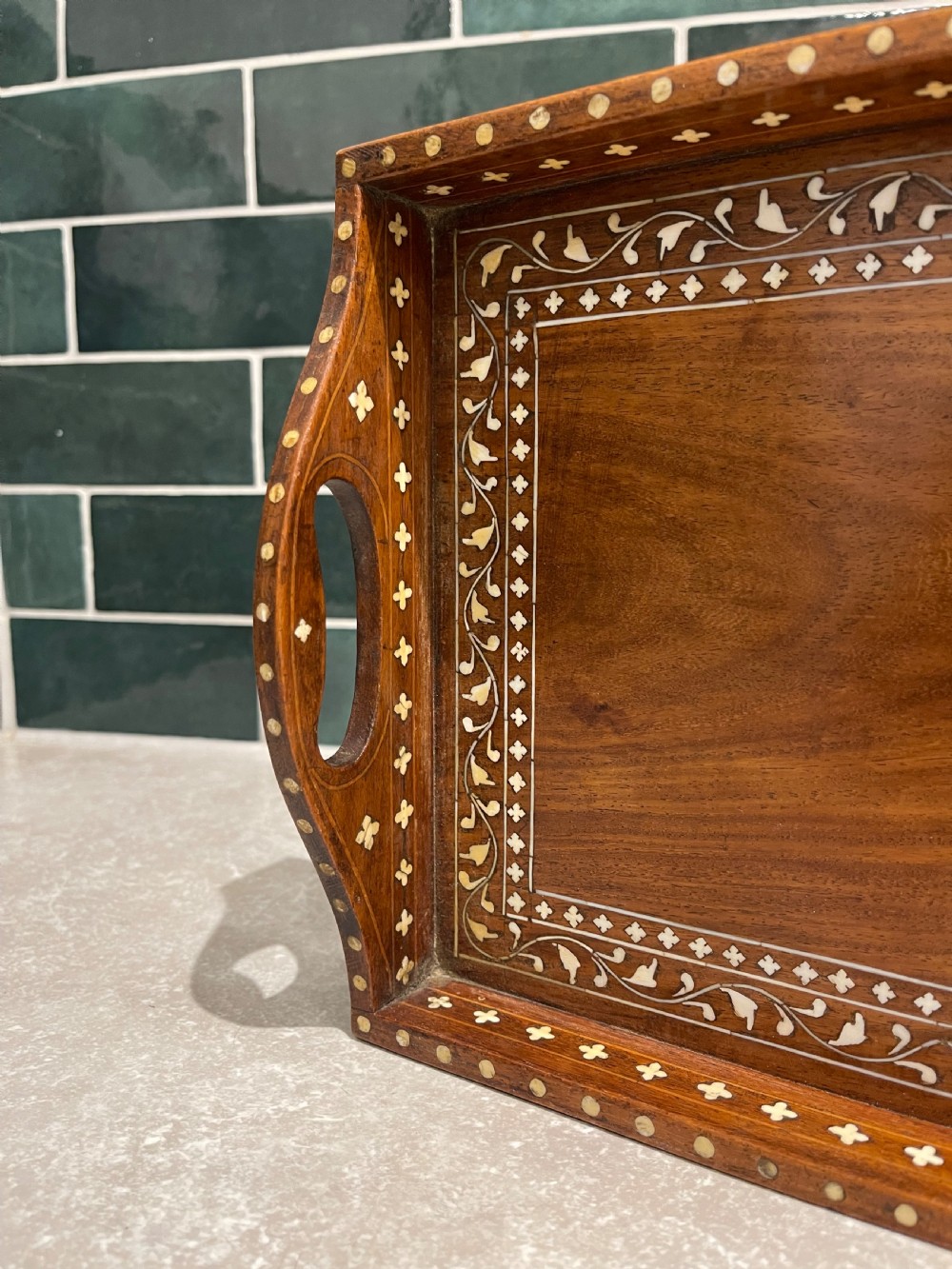 A rectangular warm brown wooden tray featuring intricate white bone inlay in a central floral rosette motif and surrounding foliate borders with cut-out handles. View IV