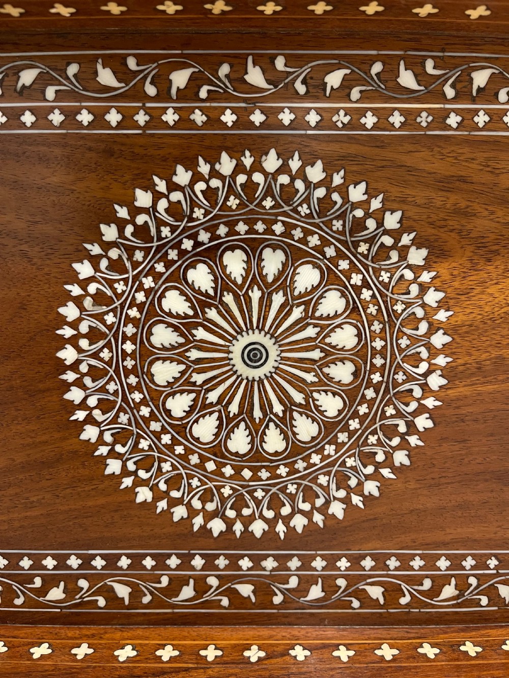 A rectangular warm brown wooden tray featuring intricate white bone inlay in a central floral rosette motif and surrounding foliate borders with cut-out handles. View V