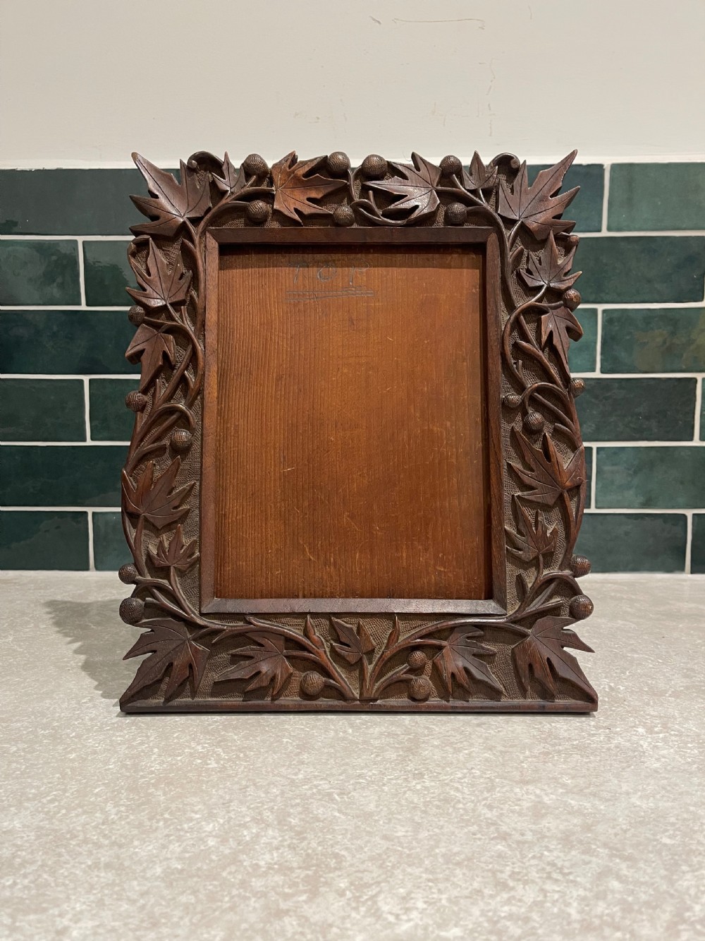 A hand-carved dark walnut picture frame featuring a relief border of chinar leaves and seed pods against a textured stippled background.