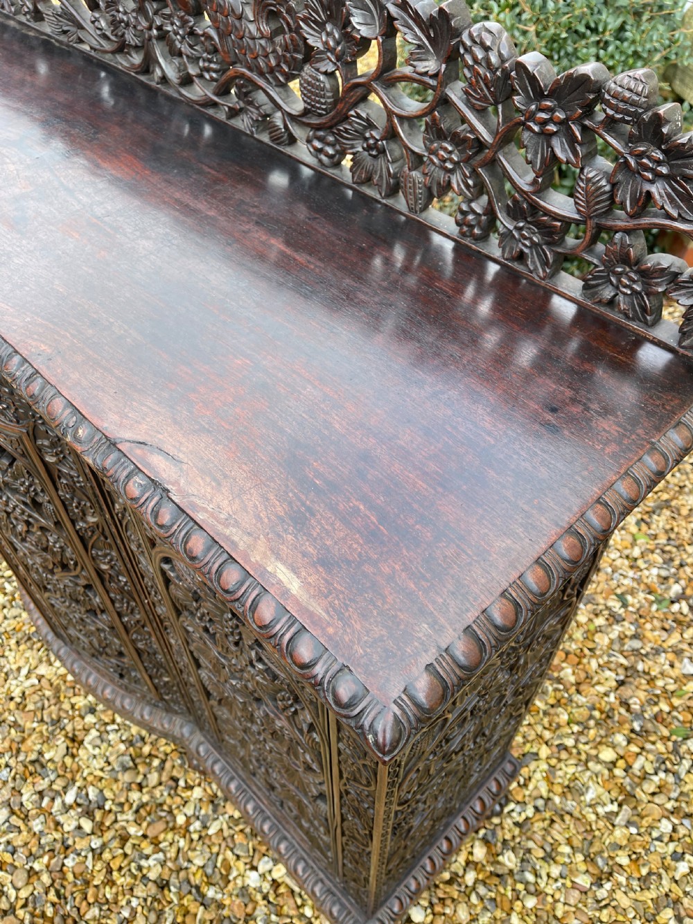 A dark carved padauk sideboard featuring four pierced floral fretwork doors, a carved gallery backrest, and bun feet. View VII