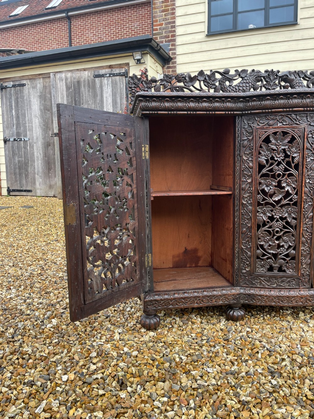 A dark carved padauk sideboard featuring four pierced floral fretwork doors, a carved gallery backrest, and bun feet. View X