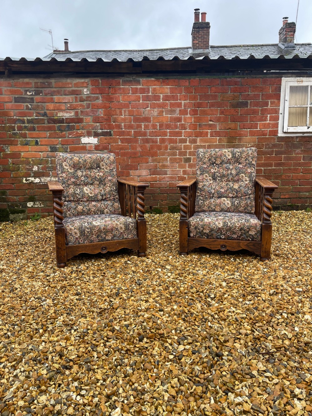 A pair of oak reclining armchairs with floral upholstered cushions, barley twist front arm supports, and slatted side panels.