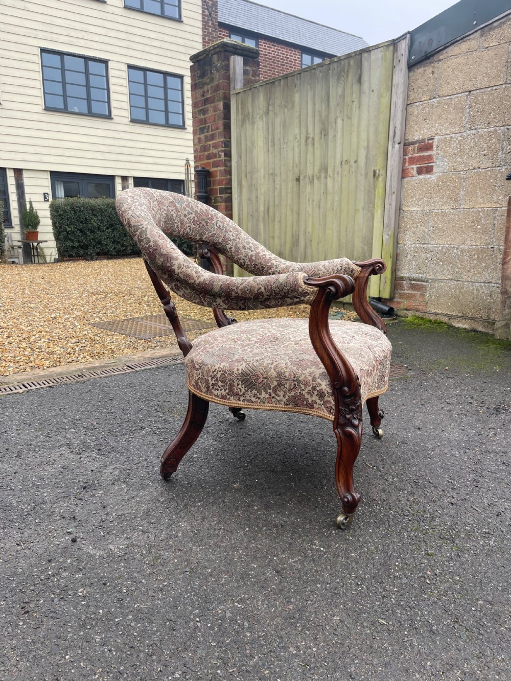 An early Victorian tub armchair crafted from dark carved rosewood with scroll armrests, cabriole legs on brass castors, and upholstered in a patterned beige floral fabric. View II