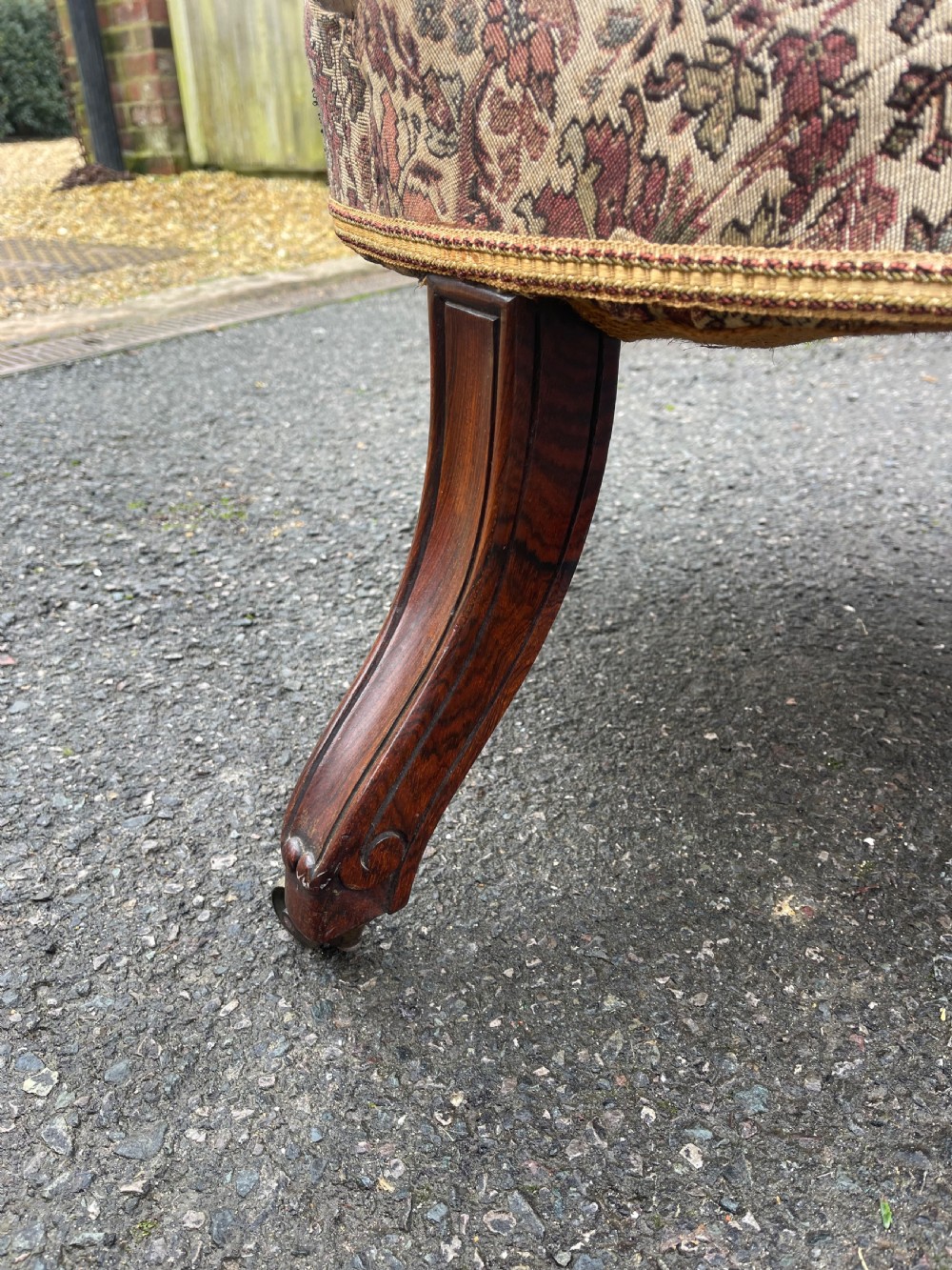 An early Victorian tub armchair crafted from dark carved rosewood with scroll armrests, cabriole legs on brass castors, and upholstered in a patterned beige floral fabric. View III