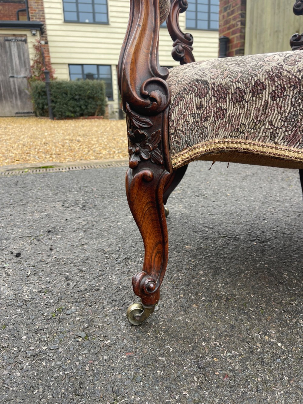 An early Victorian tub armchair crafted from dark carved rosewood with scroll armrests, cabriole legs on brass castors, and upholstered in a patterned beige floral fabric. View IV