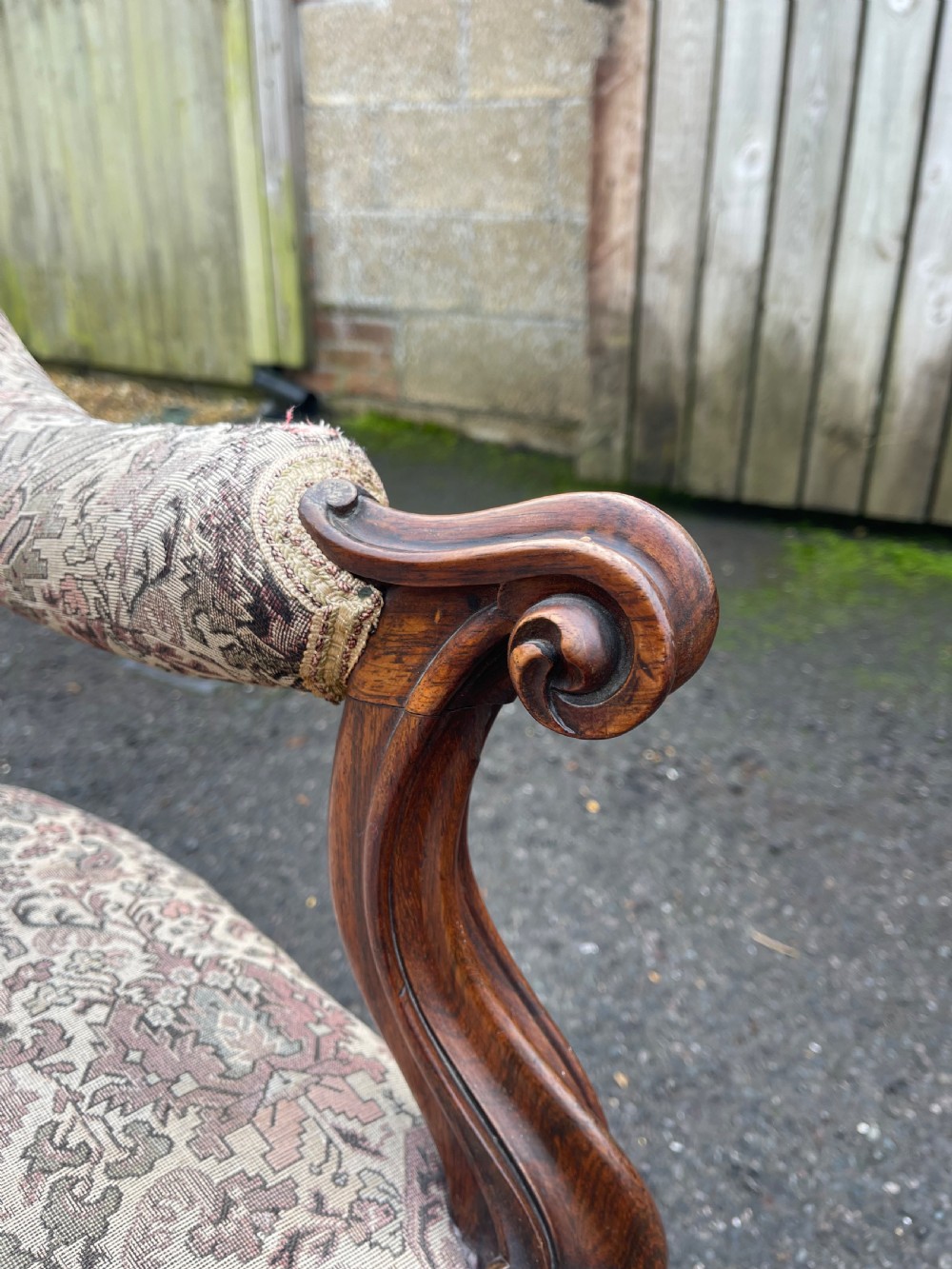 An early Victorian tub armchair crafted from dark carved rosewood with scroll armrests, cabriole legs on brass castors, and upholstered in a patterned beige floral fabric. View V