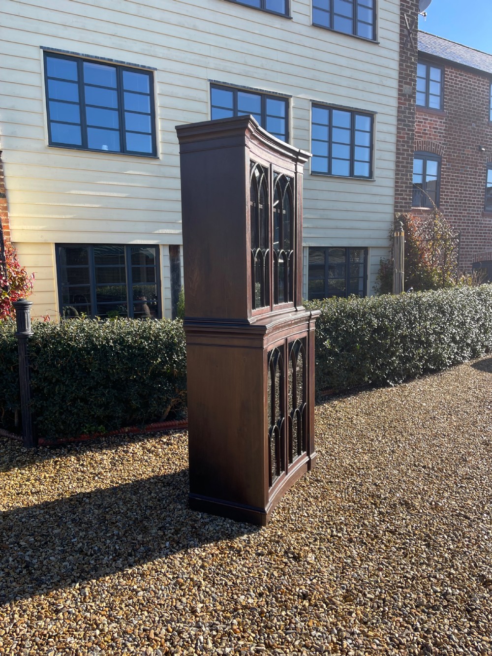 A tall dark mahogany two-door glazed bookcase featuring a concave front facade and gothic pointed arch glazing bars. View II