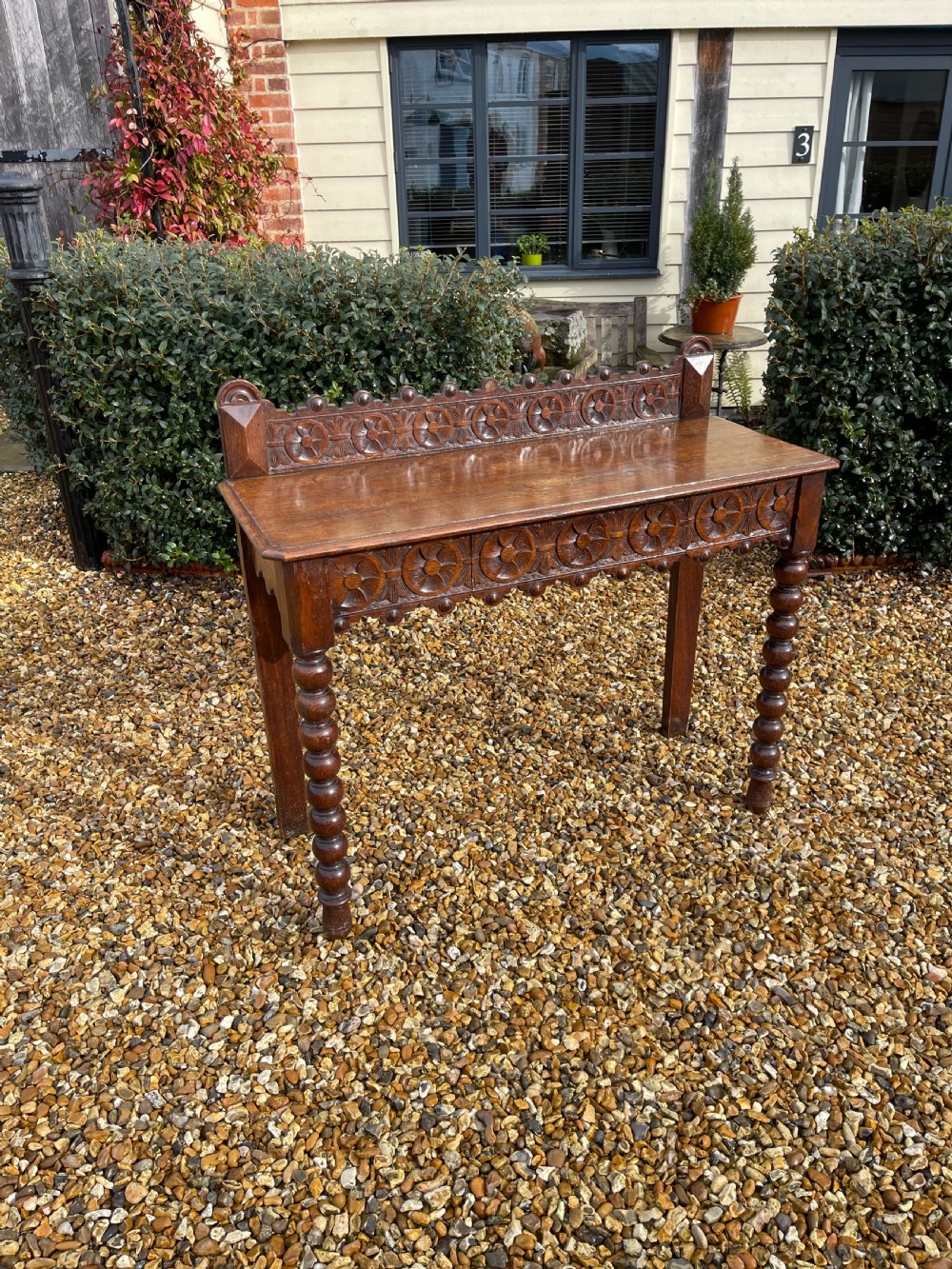 A Victorian oak hall table featuring a carved rosette gallery back, decorative apron, and front bobbin-turned legs.
