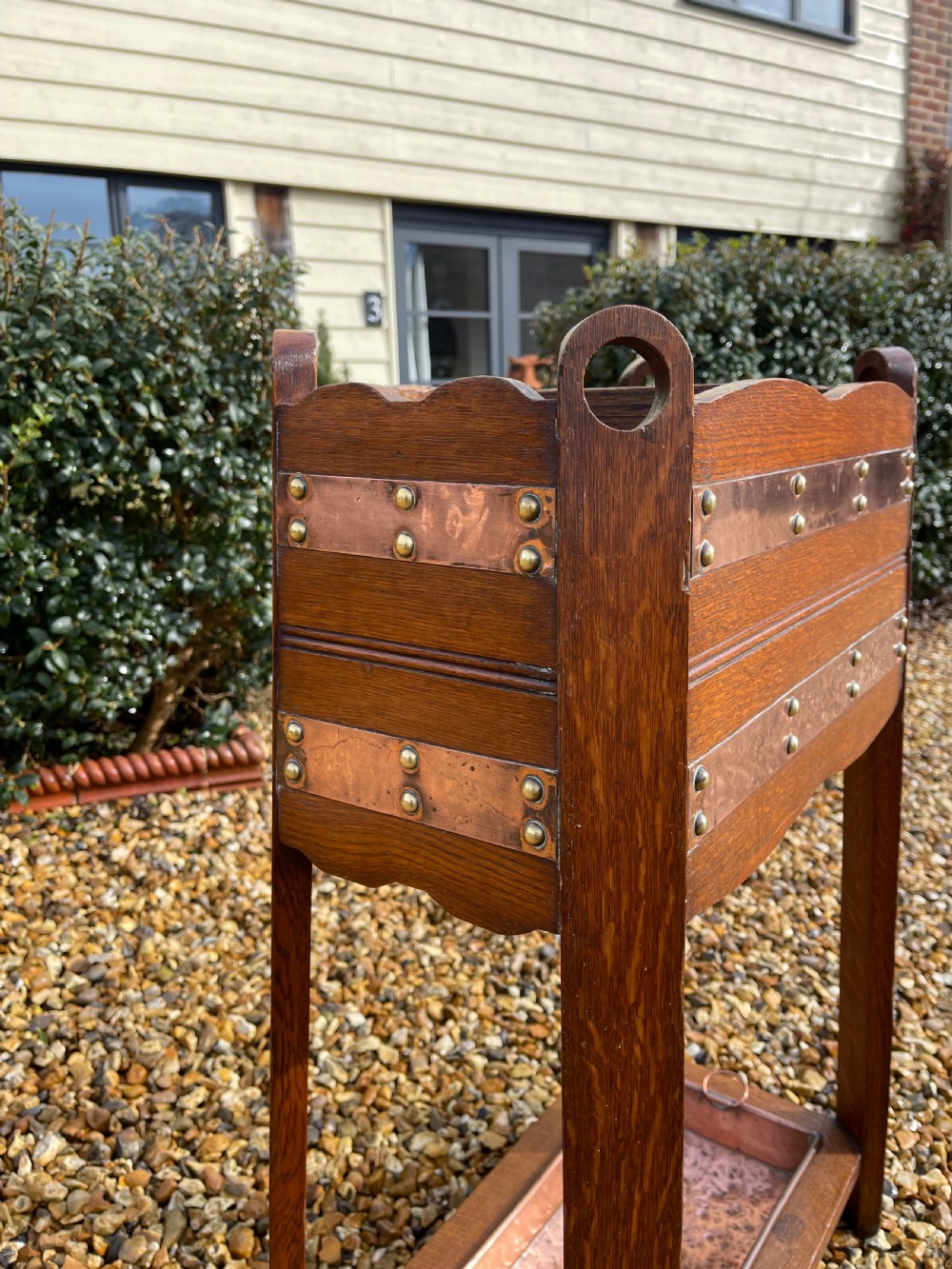 An oak Arts and Crafts umbrella stand featuring hammered copper bands, circular pierced side handles, four top compartments, and a removable copper drip tray at the base. View II