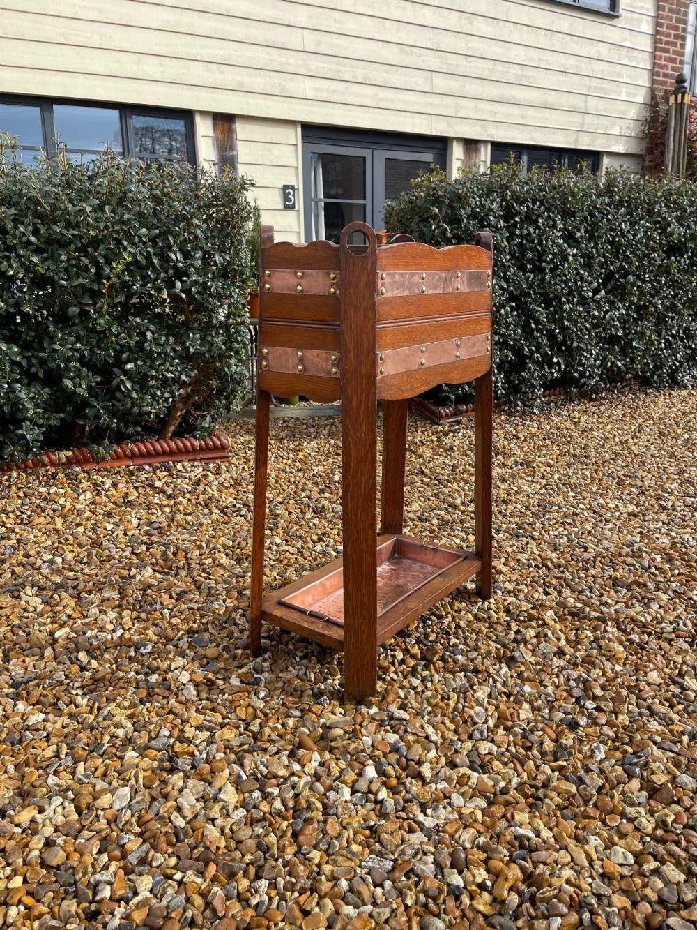 An oak Arts and Crafts umbrella stand featuring hammered copper bands, circular pierced side handles, four top compartments, and a removable copper drip tray at the base. View III