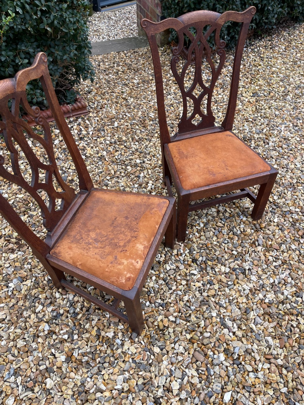 A pair of dark oak antique side chairs with intricately carved openwork back splats and tan upholstered seats. View VI