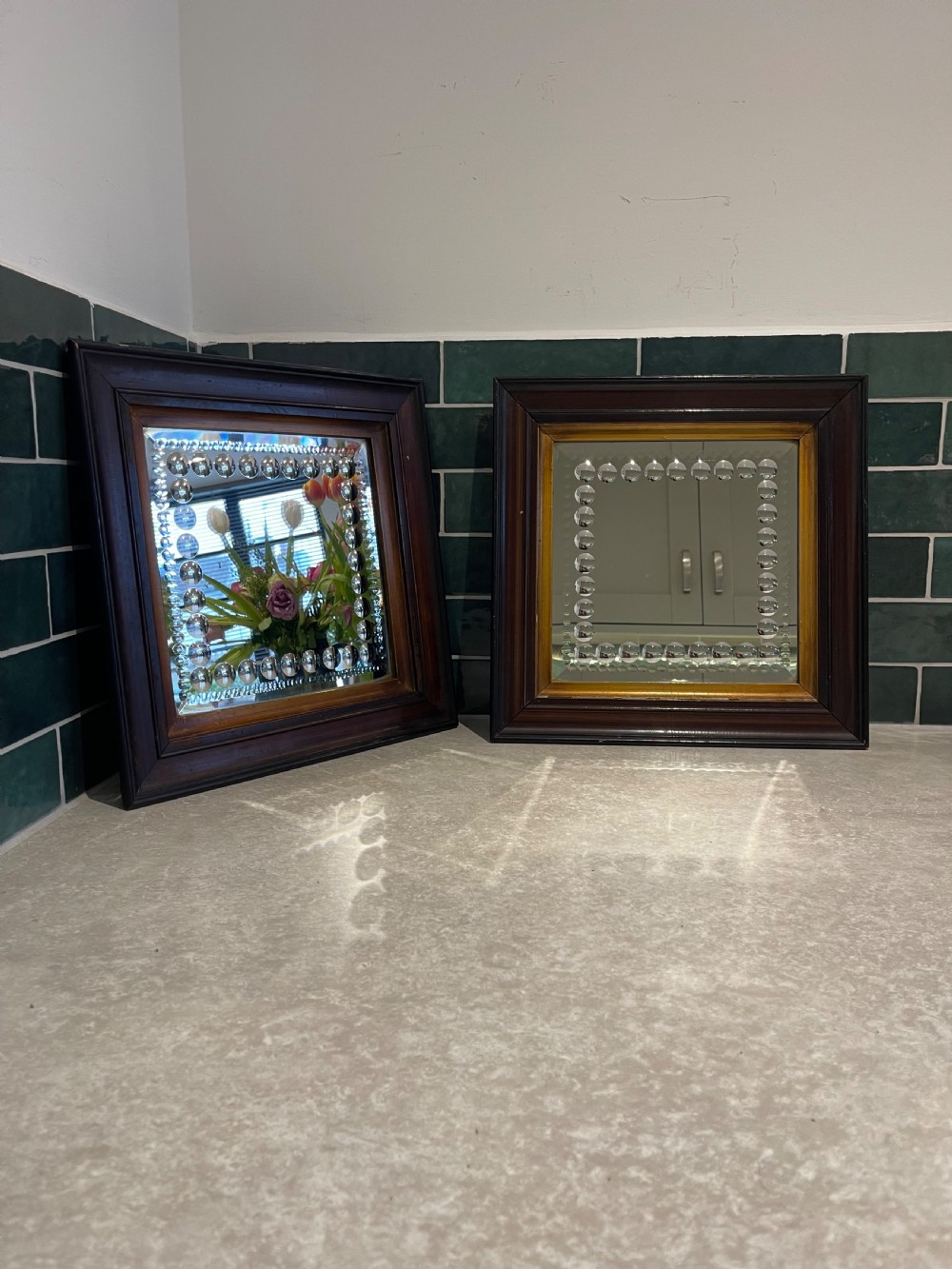 A pair of square dark wood framed mirrors featuring a border of convex glass studs surrounding the central mirrored glass panel.