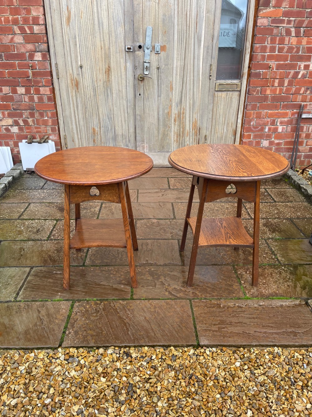 A pair of matching Arts and Crafts style oak side tables with circular tops, pierced heart motif friezes, and lower undertier shelves.