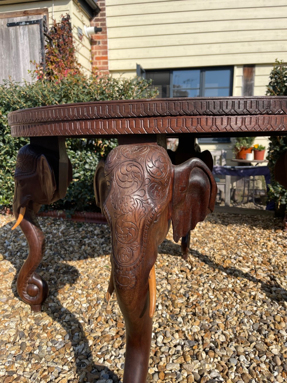 A circular carved dark wood table featuring legs shaped as elephant heads with tusks and an inset circular engraved brass tray in the centre. View II