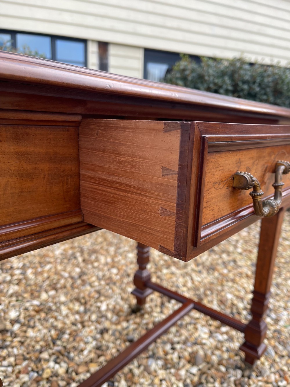 A Victorian inlaid mahogany writing table featuring a single drawer with brass drop handles, floral marquetry, square tapered legs, and an H-stretcher base. View IV