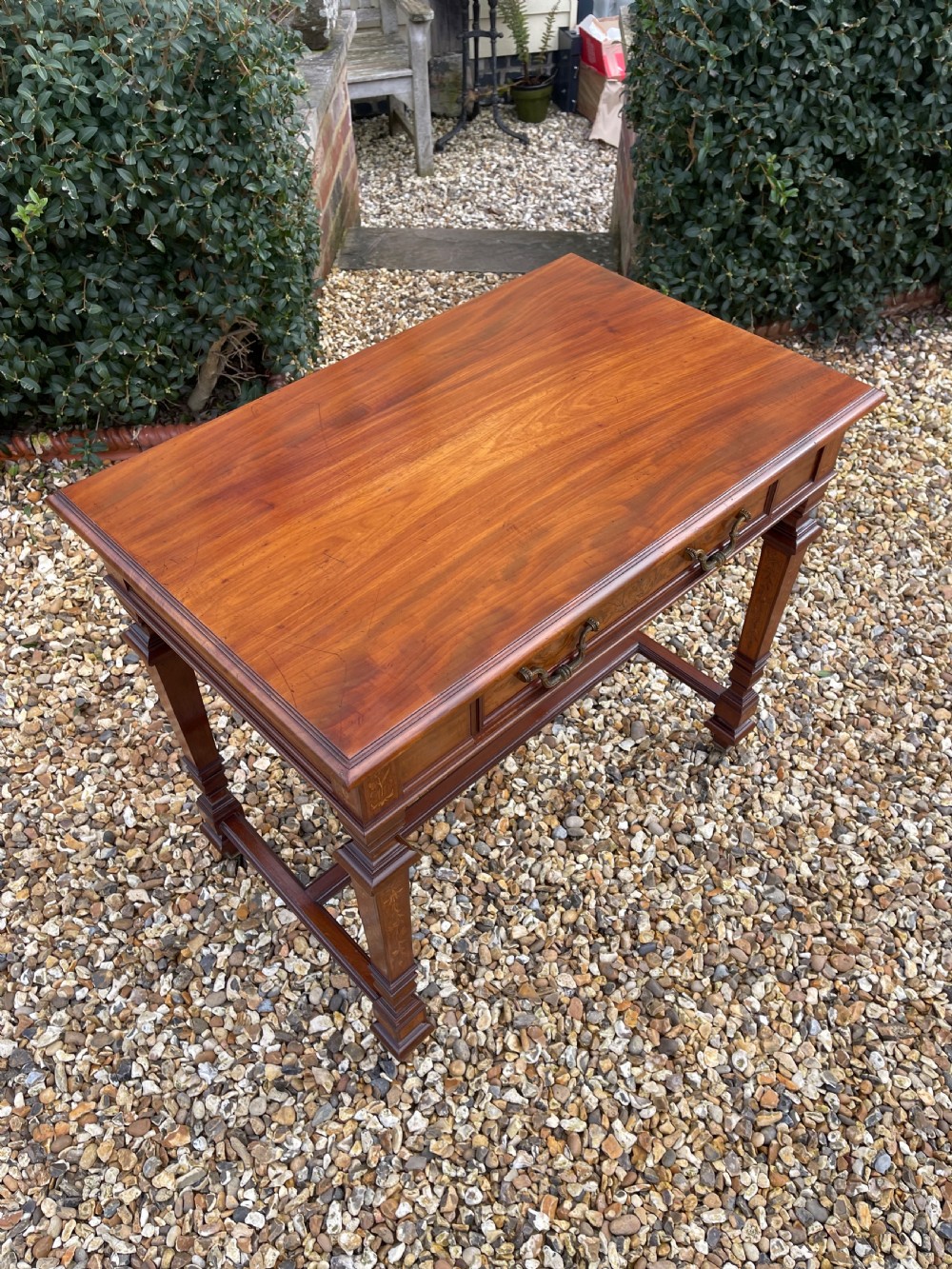 A Victorian inlaid mahogany writing table featuring a single drawer with brass drop handles, floral marquetry, square tapered legs, and an H-stretcher base. View V