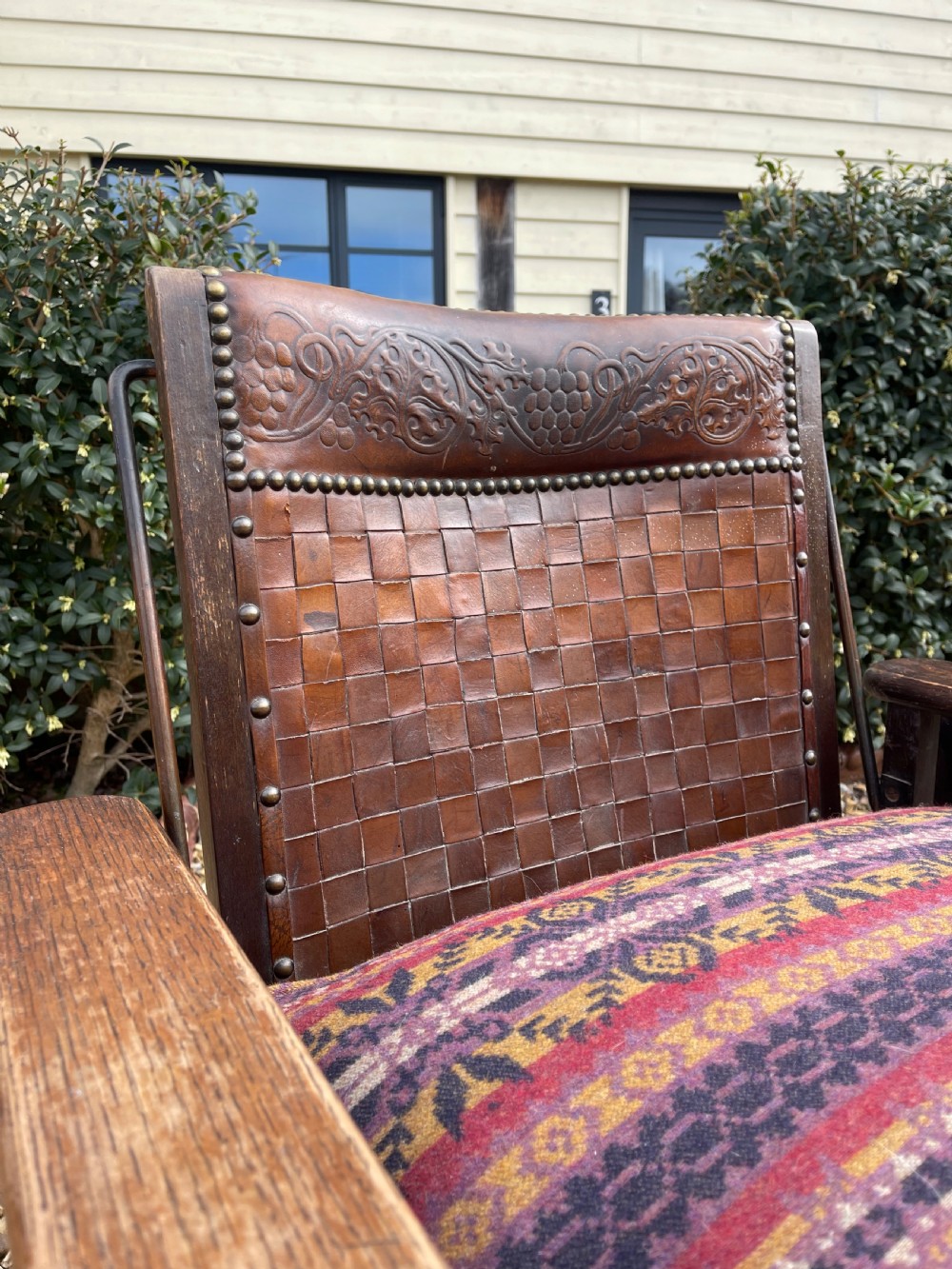 An antique Arts and Crafts oak reclining armchair featuring wide flat armrests, a woven leather back, caned sides, and a pattern-upholstered cushion. View II