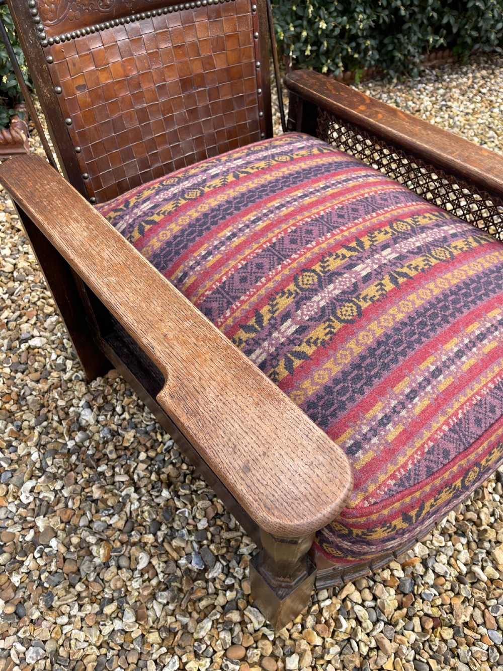 An antique Arts and Crafts oak reclining armchair featuring wide flat armrests, a woven leather back, caned sides, and a pattern-upholstered cushion. View III