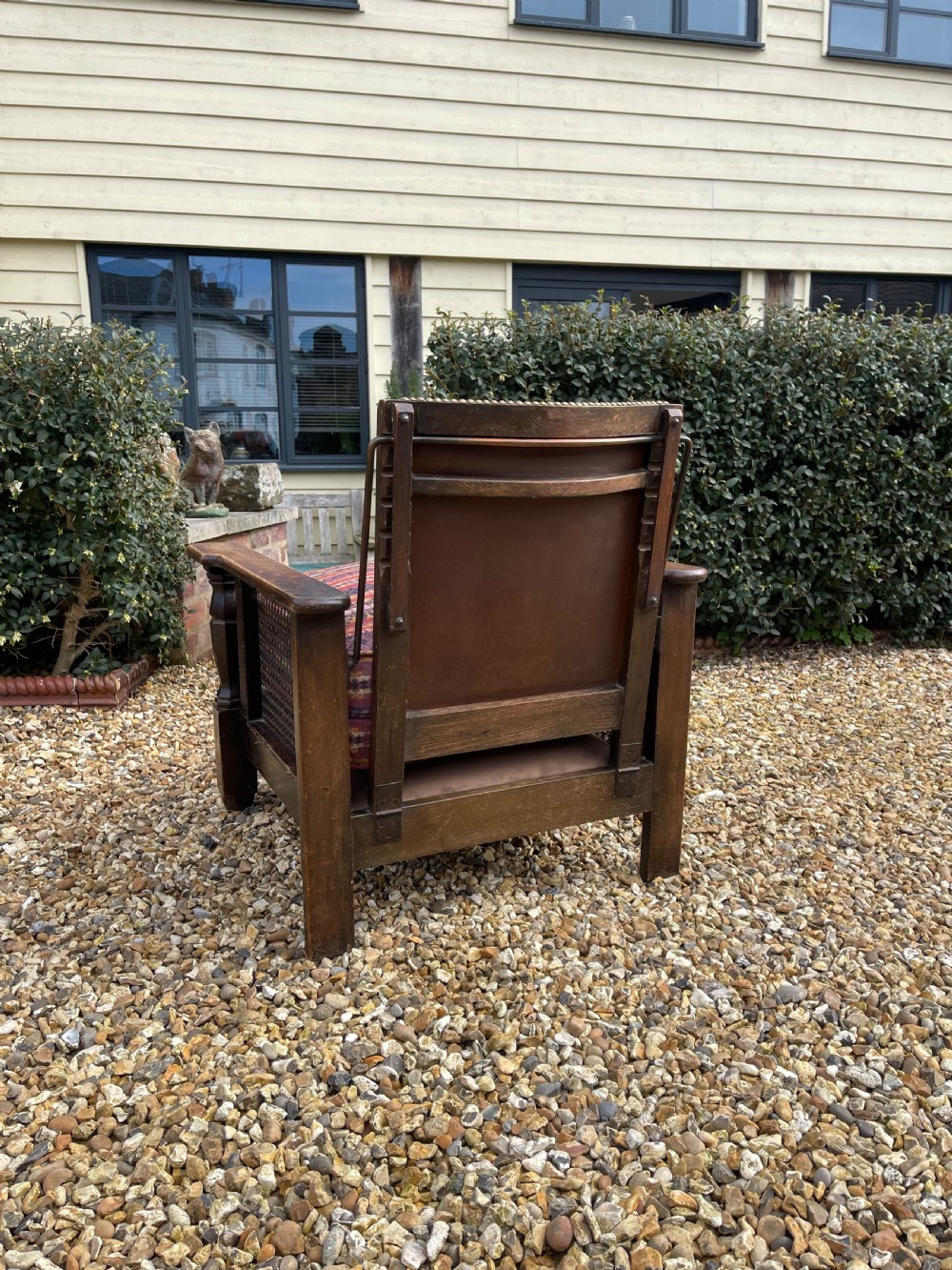 An antique Arts and Crafts oak reclining armchair featuring wide flat armrests, a woven leather back, caned sides, and a pattern-upholstered cushion. View IV