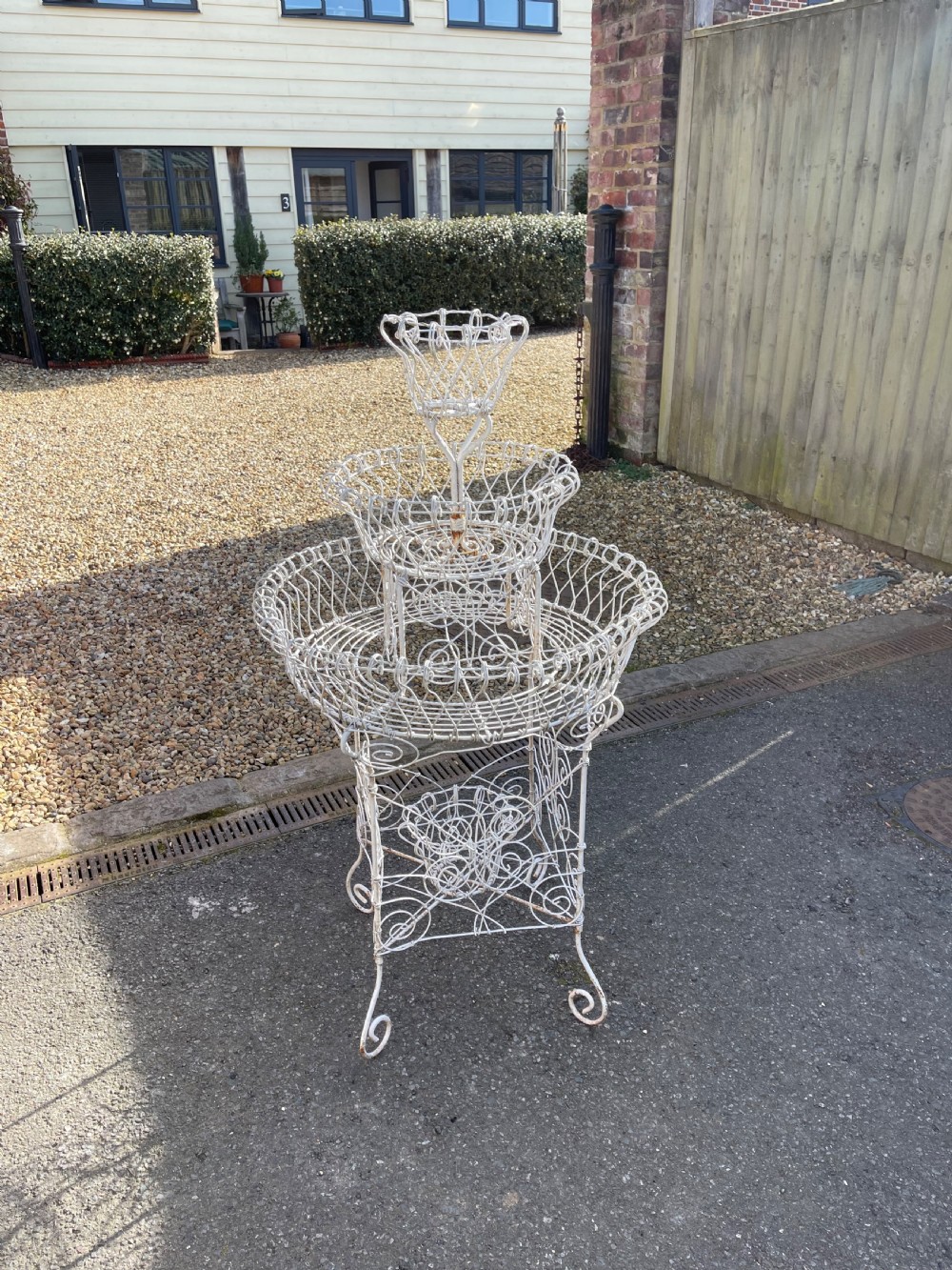 A three-tiered white painted wirework plant stand featuring scrolled feet and openwork wire baskets.