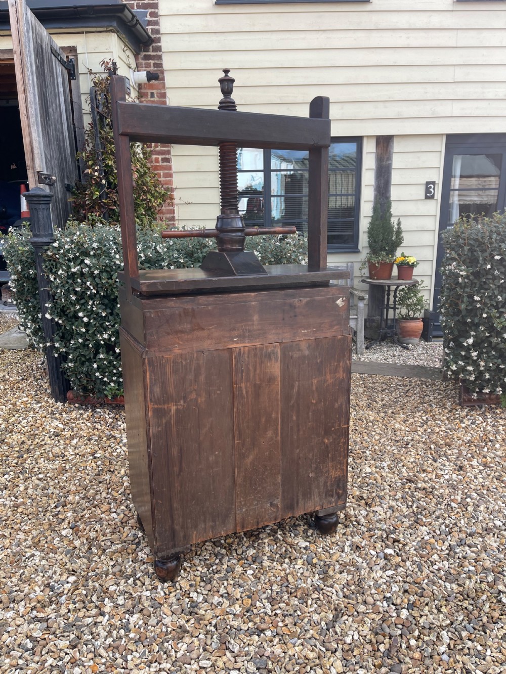 A dark oak press chest with four graduated drawers, turned knobs, bun feet, and a top-mounted wooden screw mechanism. View II