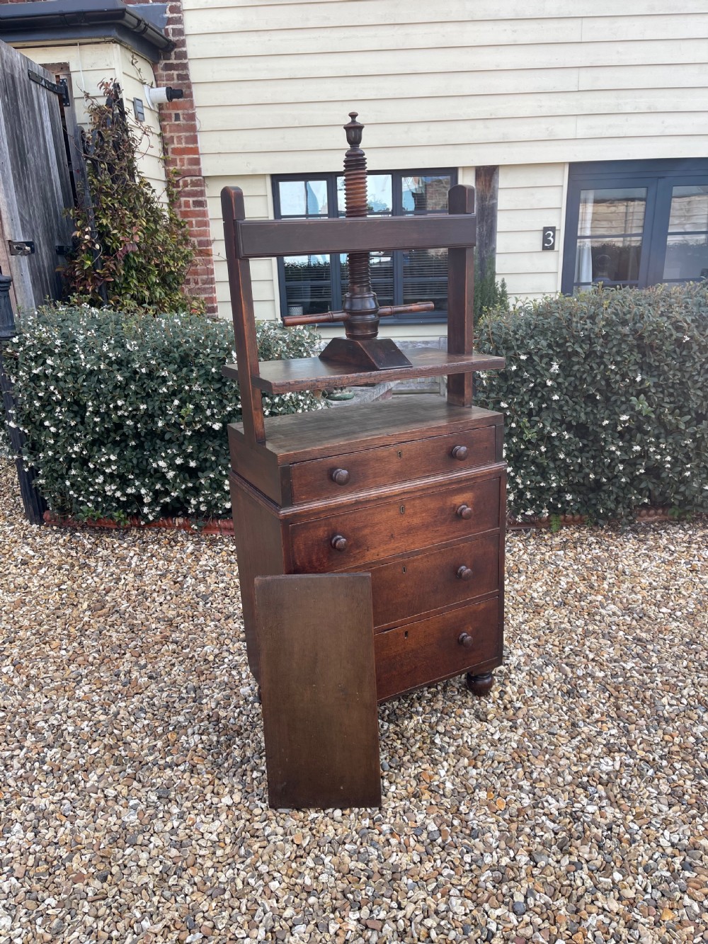 A dark oak press chest with four graduated drawers, turned knobs, bun feet, and a top-mounted wooden screw mechanism. View IV